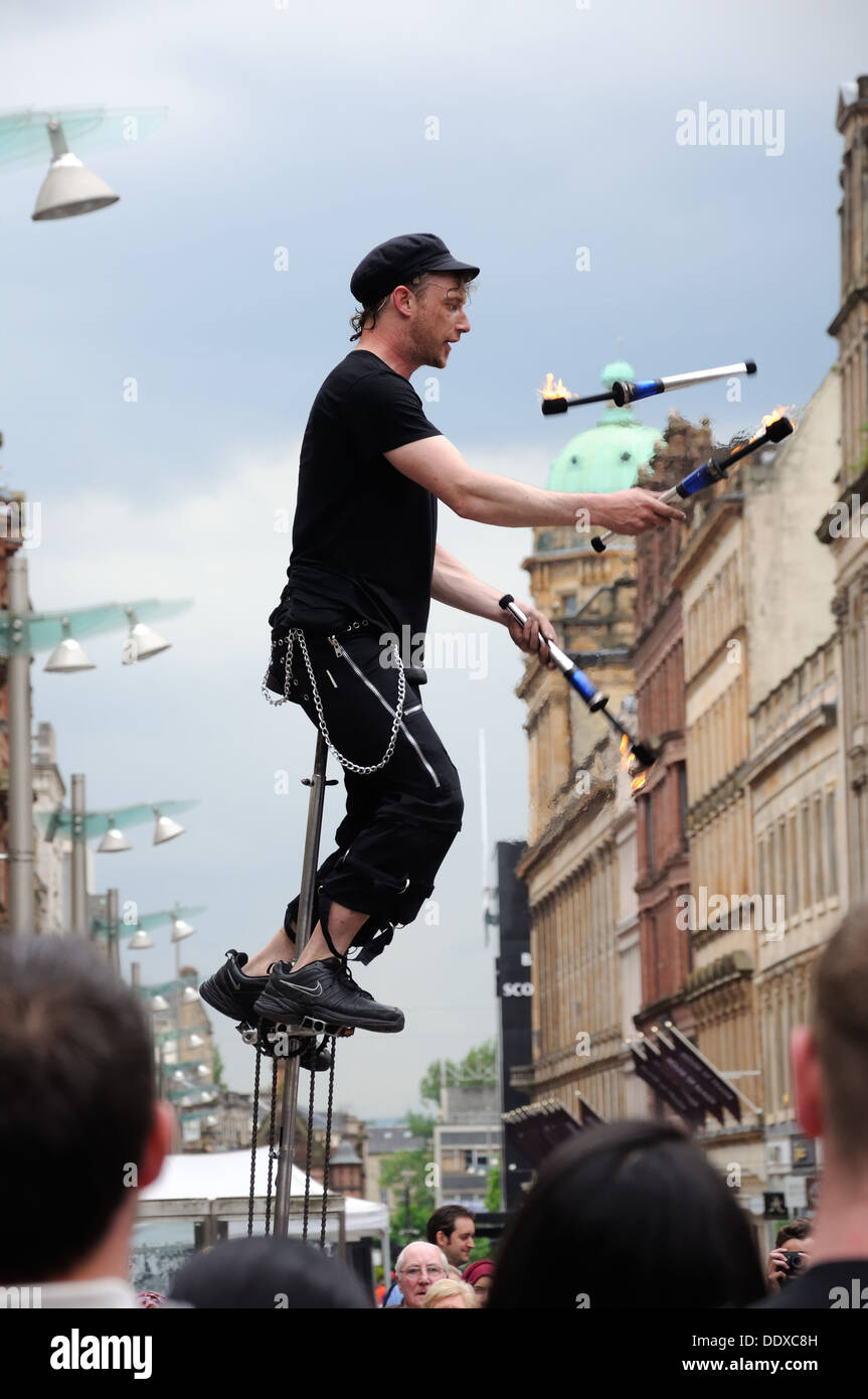 A man on a unicycle juggling lighted batons on a busy city centre precinct. Stock Photo