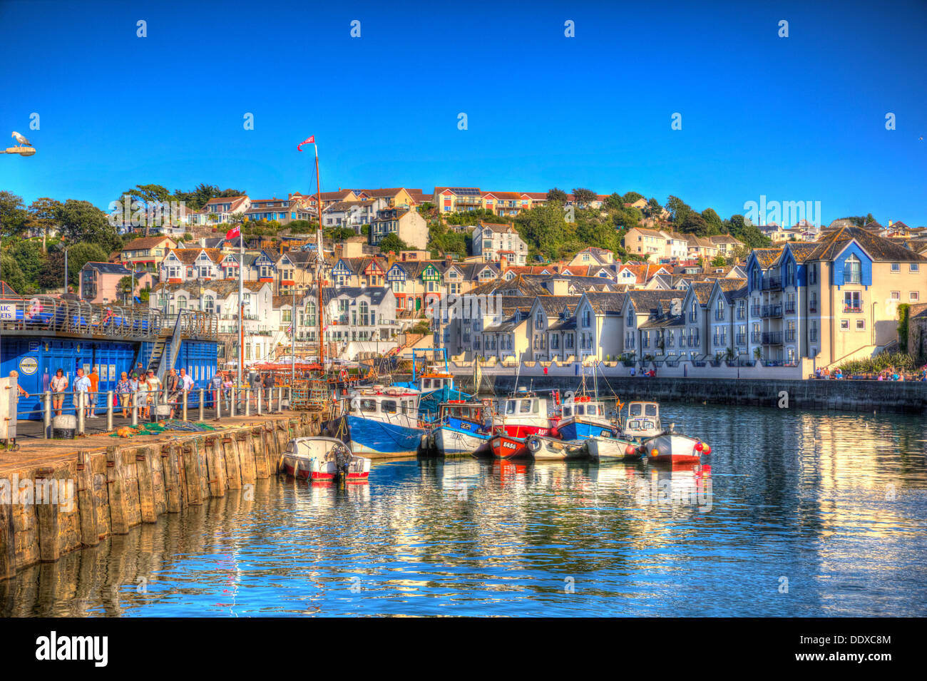 Brightly coloured boats Brixham harbour Devon with houses on hillside in background in HDR Stock Photo