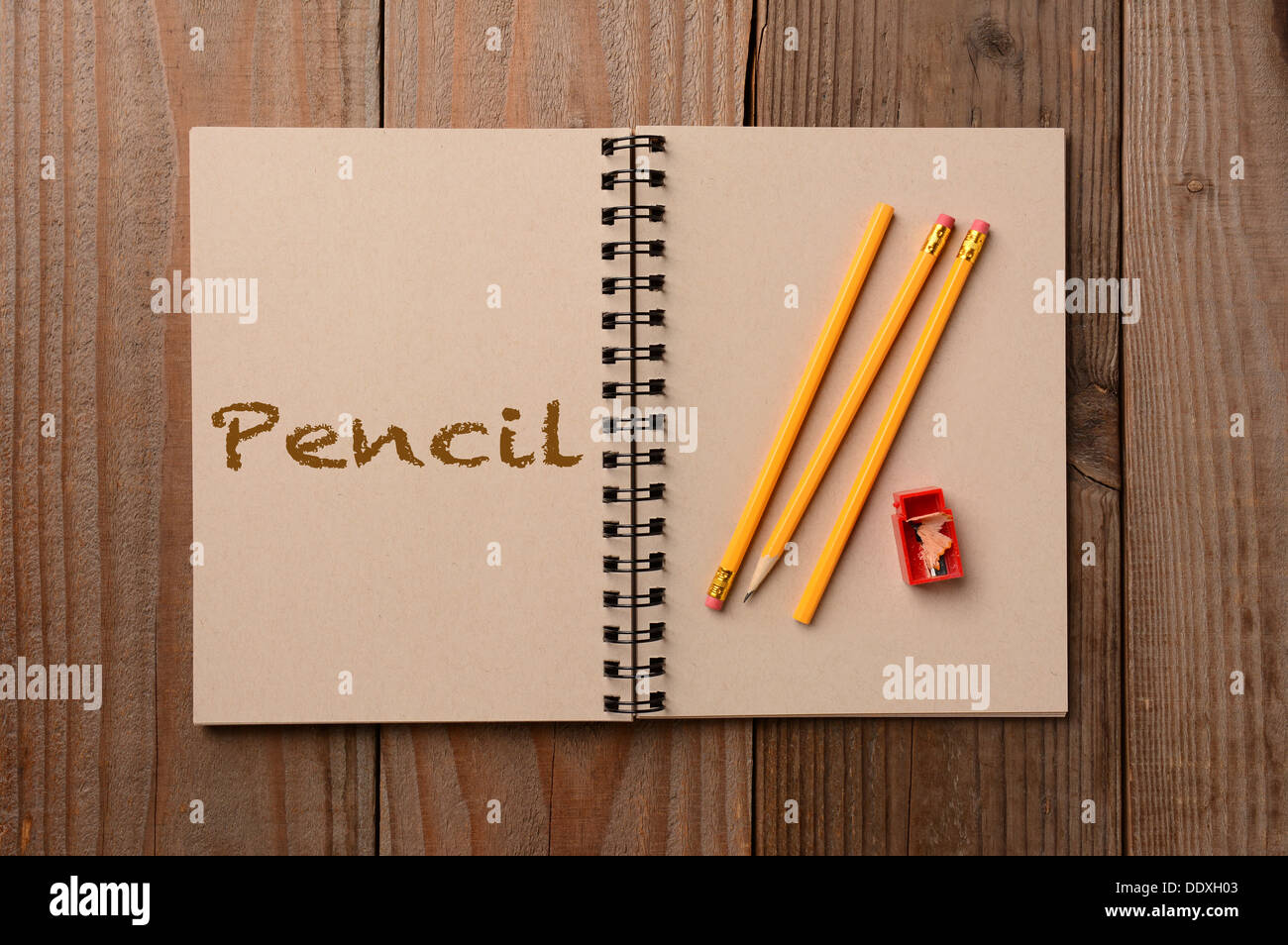 A group of pencils on the blank page of a notebook. The opposite page has the word Pencil spelled out. Stock Photo