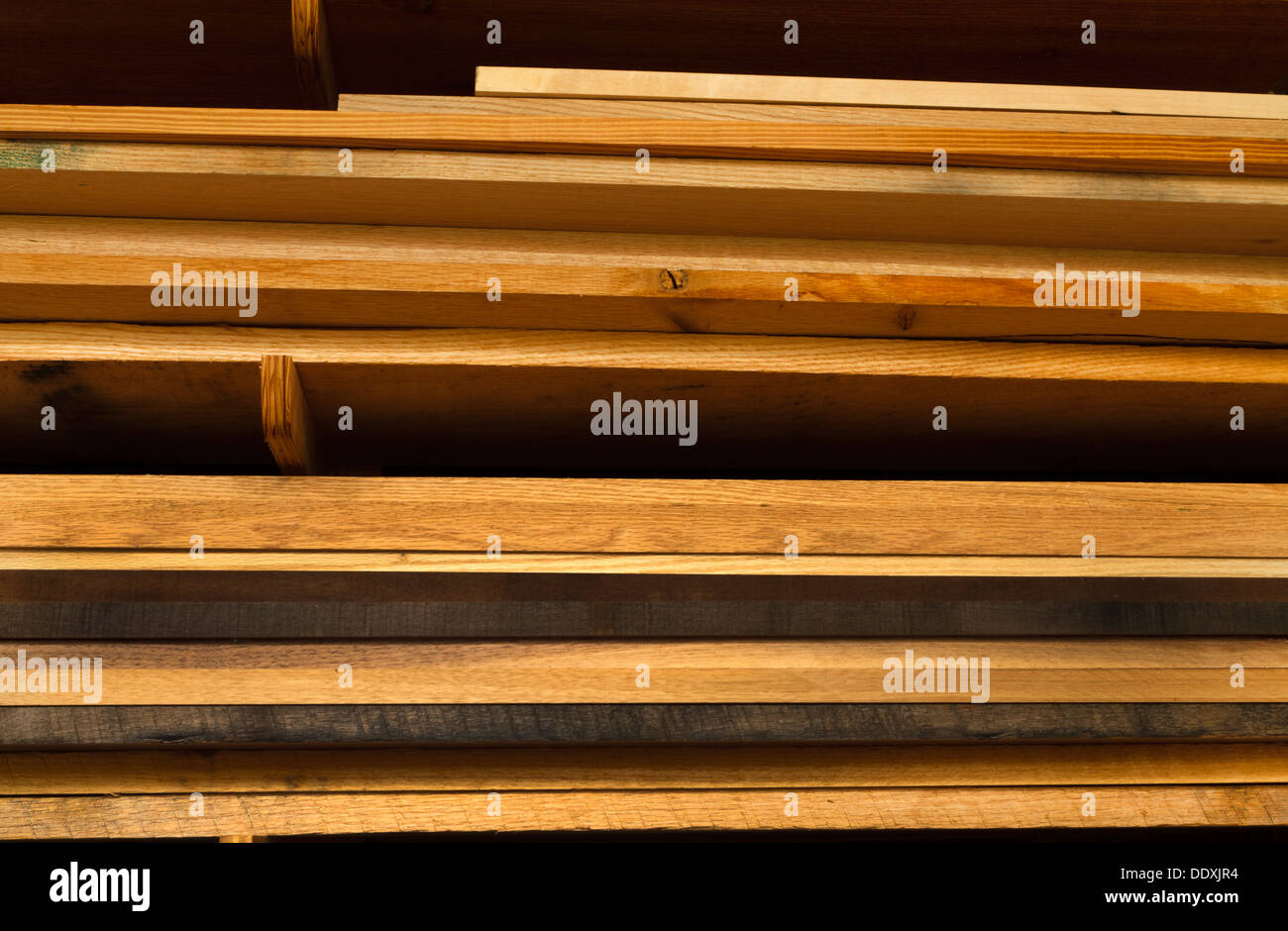 Various boards of lumber stacked on shelves in a woodworking workshop. Most of the lumber is oak wood in various stages of aging Stock Photo