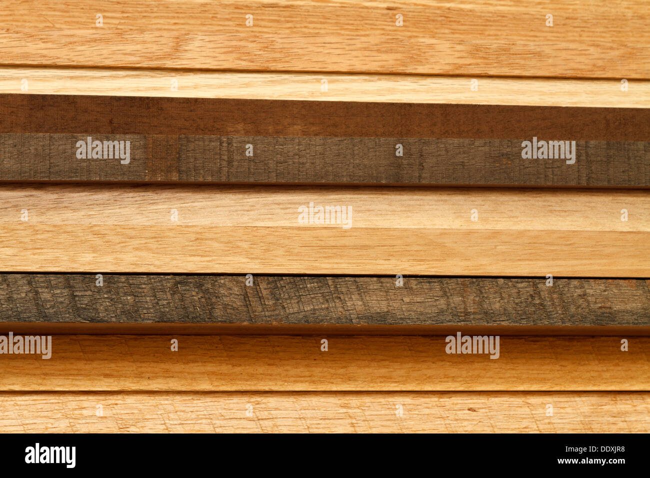 Close-up of various boards of lumber stacked from the side. Most of the lumber is oak wood in various stages of age & weathering Stock Photo
