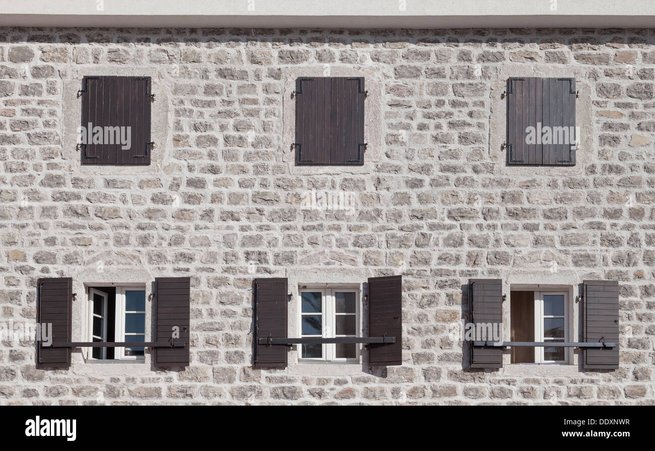Old stone building facade with dark brown windows and jalousies Stock Photo