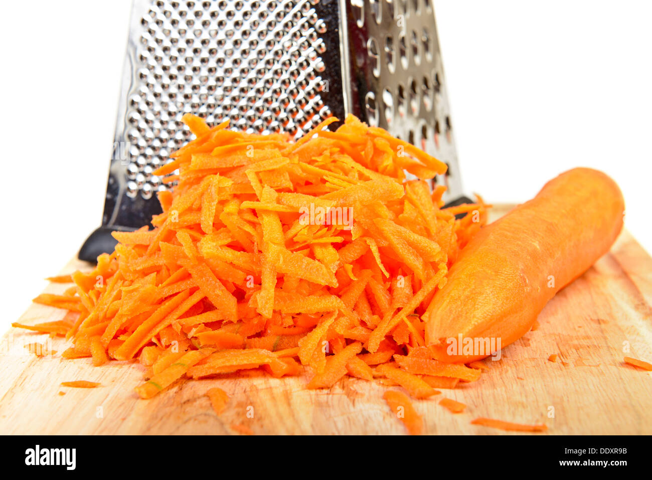 Shredded and whole carrot with metal grater on cutting board Stock Photo