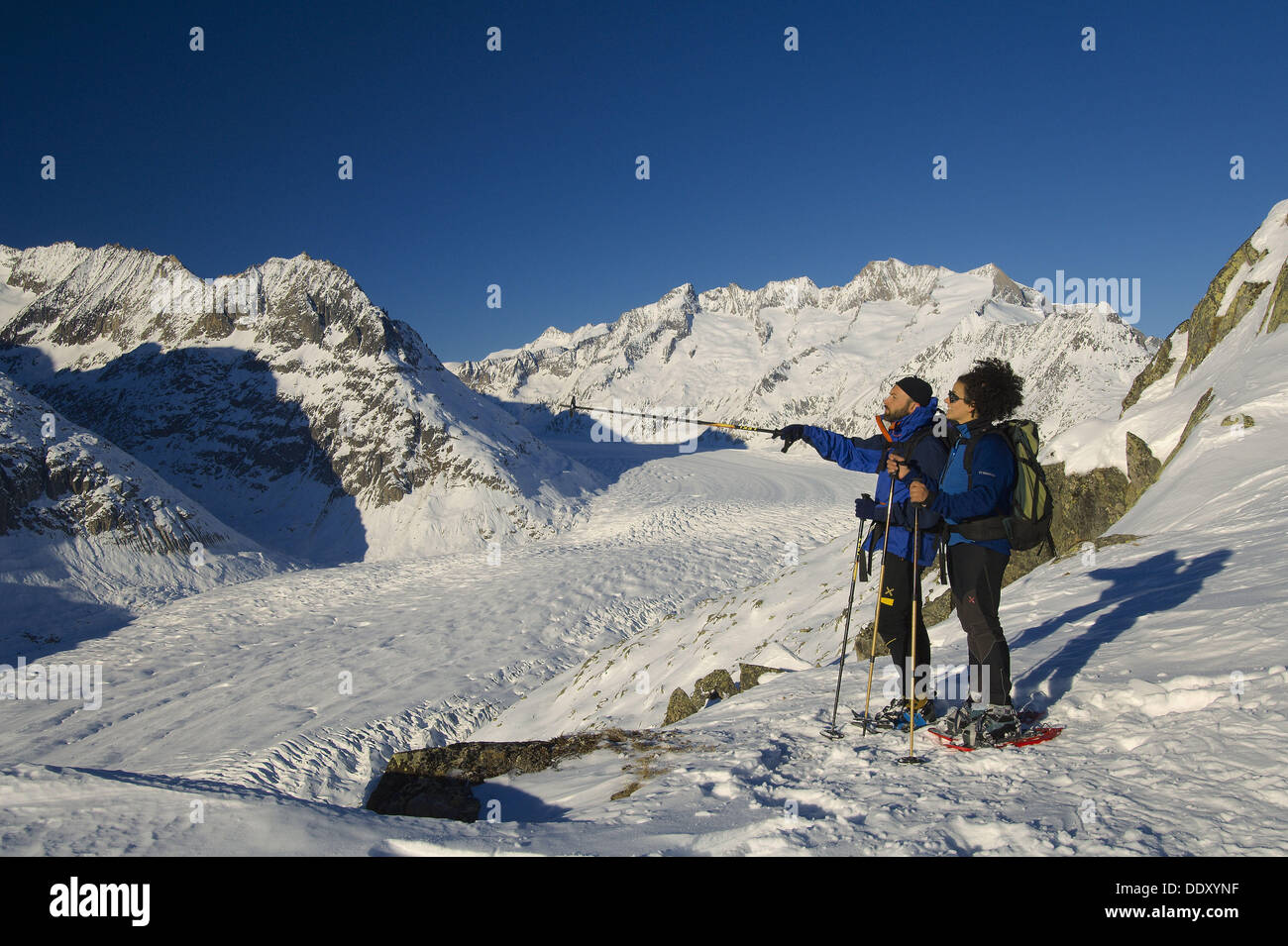 a couple of hikers walking with snowshoes in bettmerhorn with the aletsch glacier in the background bettmeralp municipality Stock Photo