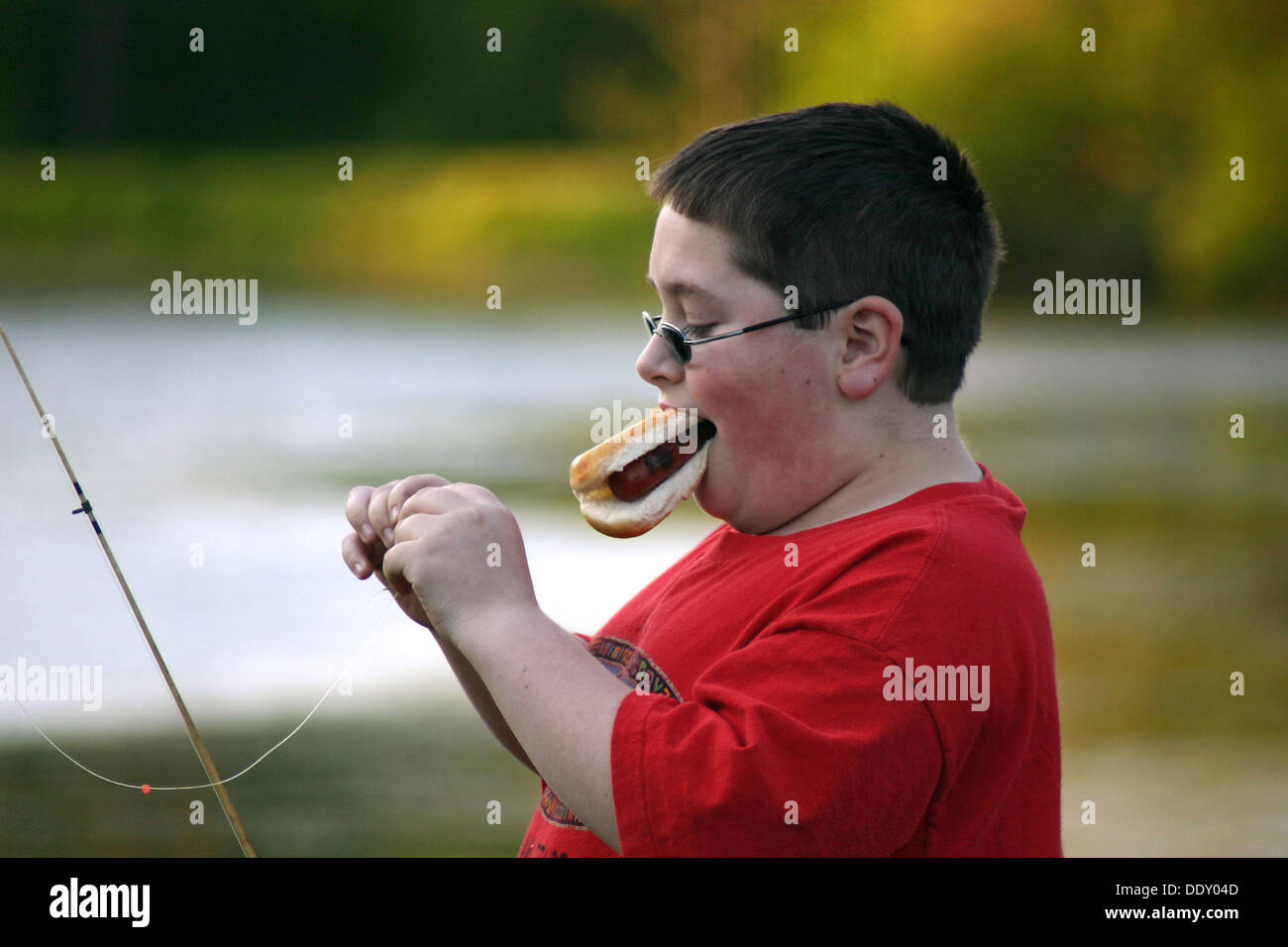 11 year old boy, eating hotdog while baiting hook for fishing ...