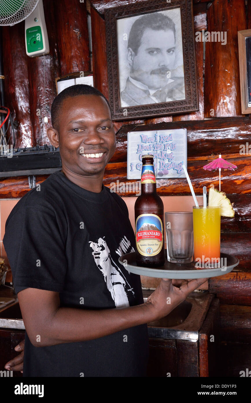 Waiter with Kilimanjaro beer and a cocktail in front of a picture of Freddy Mercury, the late singer of the rock band Queen who Stock Photo