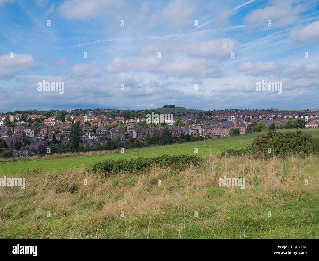 View of a town and houses from some fields in the summer set against a moody blue and cloudy sky. Stock Photo