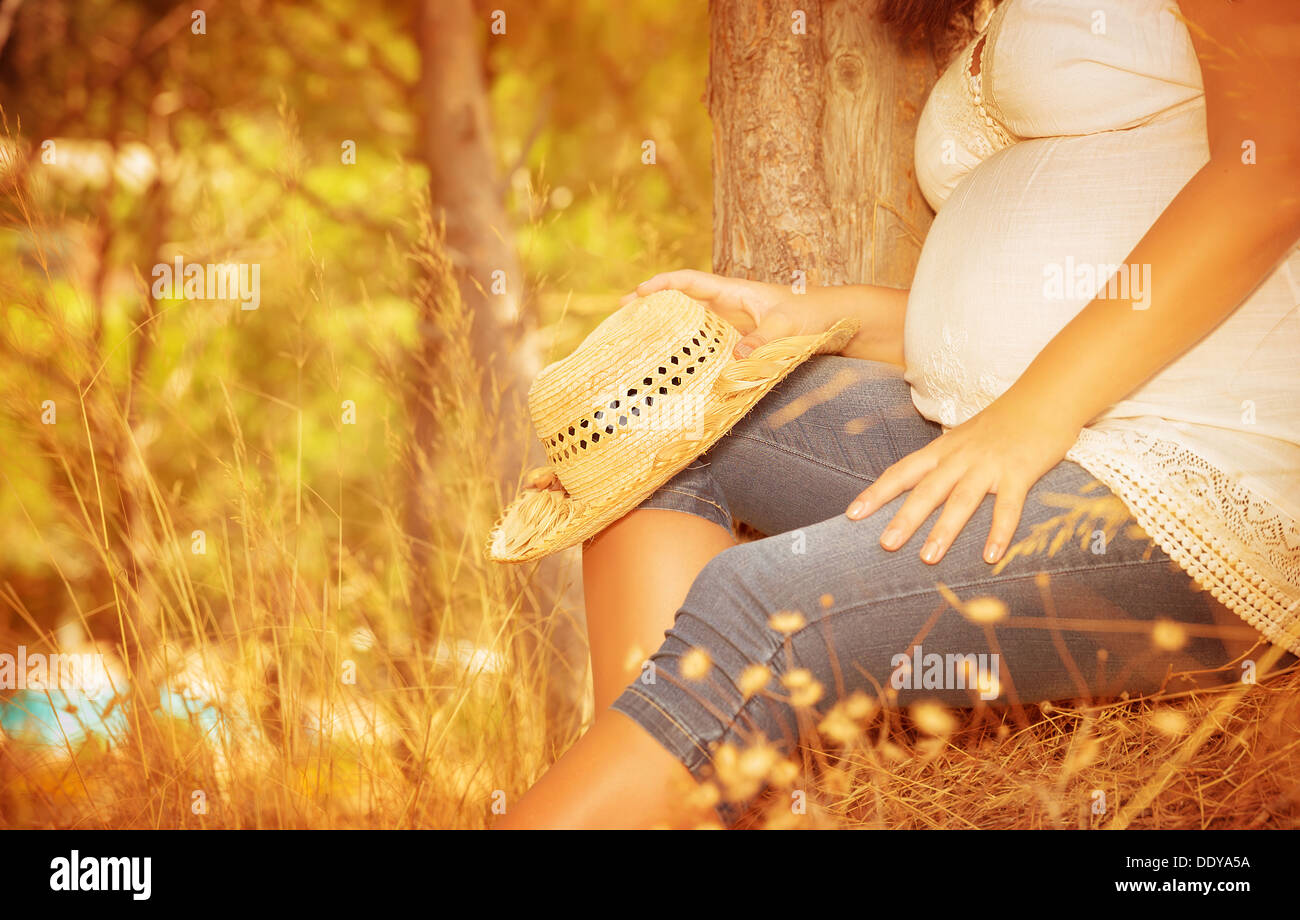 Pregnant girl sitting in autumnal park, body part, tummy of expectant woman, spending time in countryside, healthy pregnancy Stock Photo