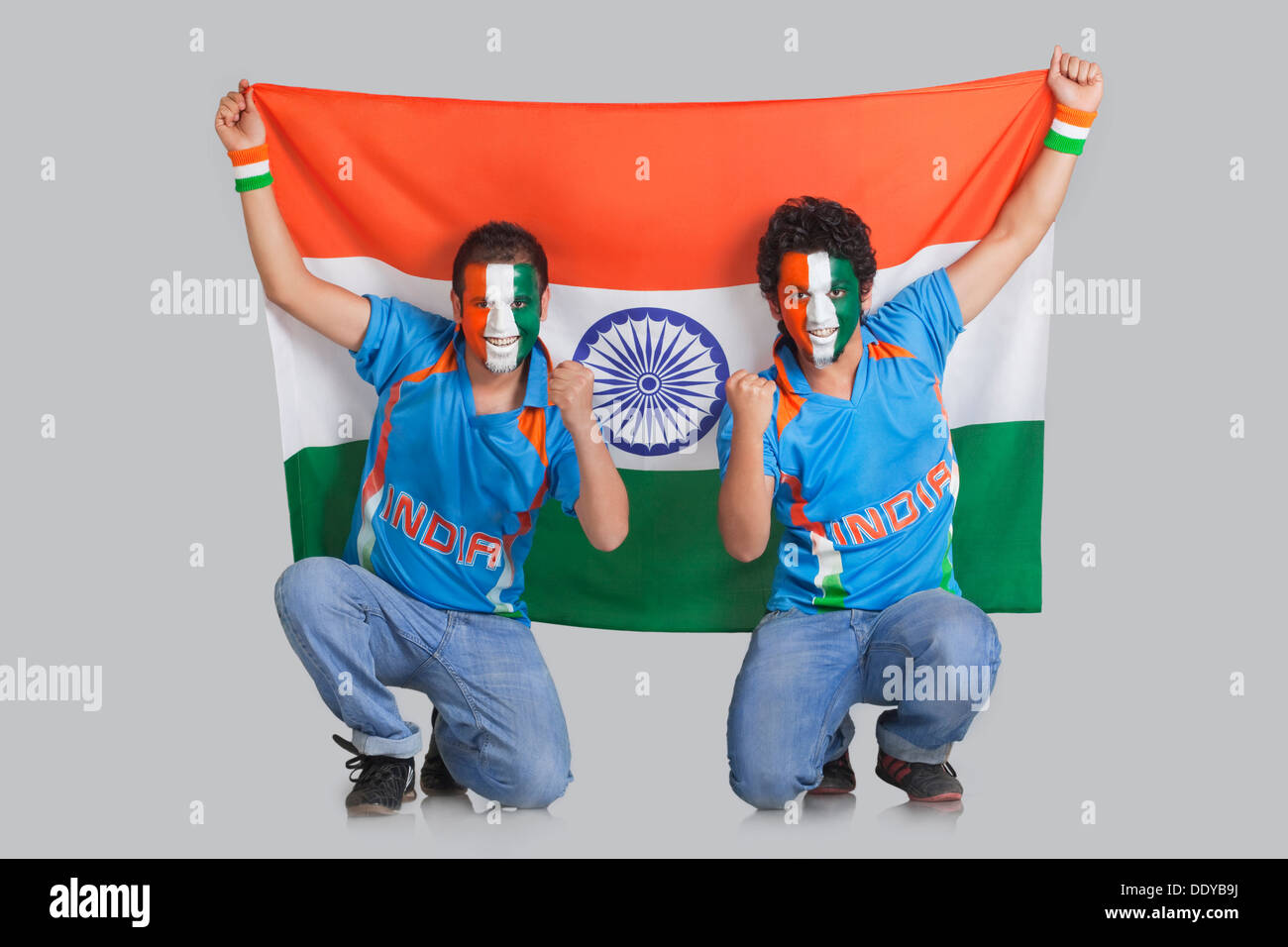 Male cricket fans with face painted in tricolor holding Indian flag over colored background Stock Photo