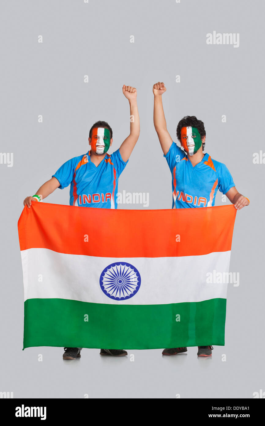Male crickets fans with face painted in tricolor holding Indian flag over colored background Stock Photo
