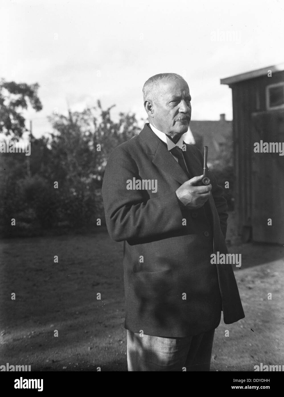 An elderly man with a starched collar, smoking a pipe in his garden, Flyinge, Sweden, 1920s. Artist: Unknown Stock Photo