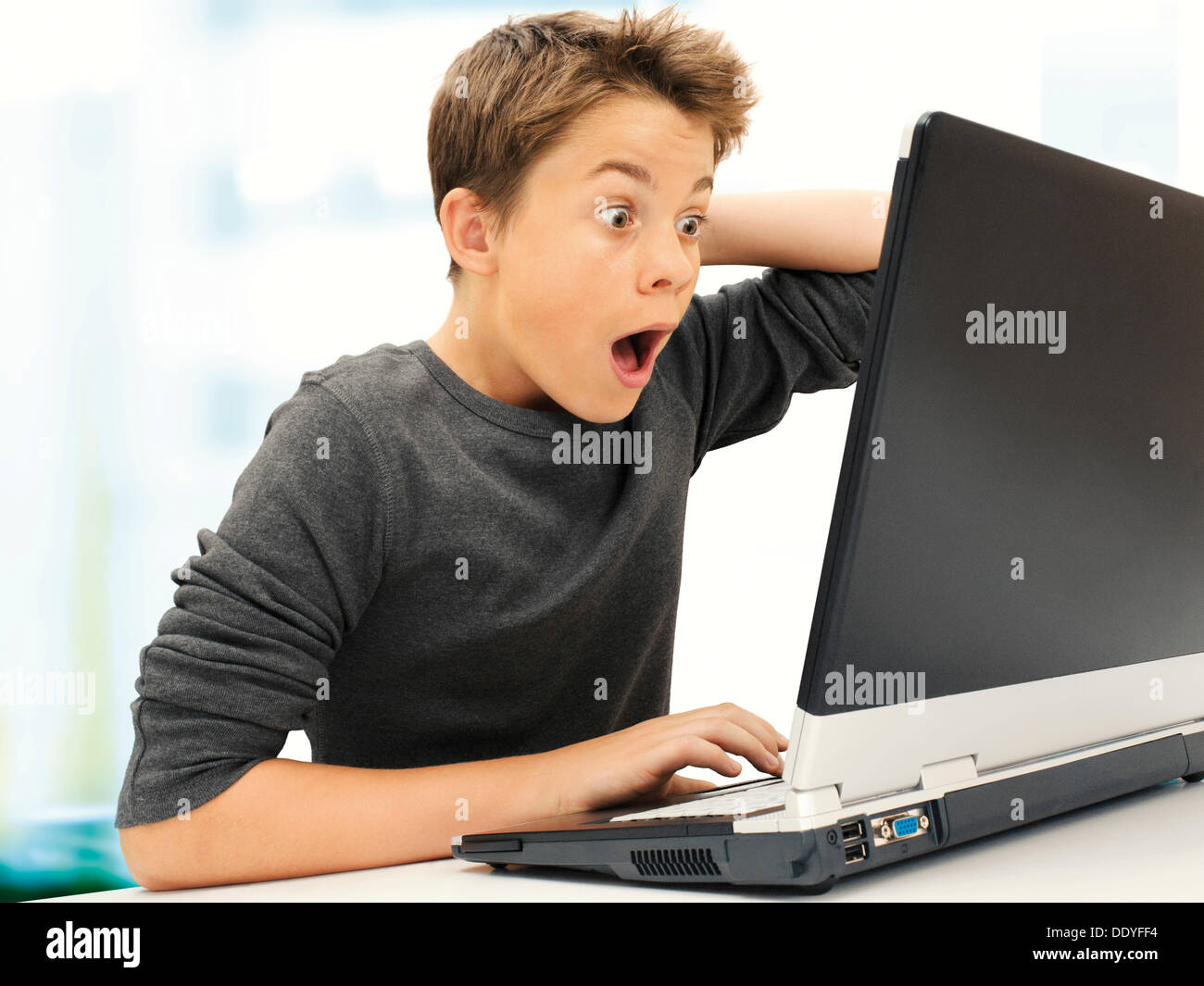 Portrait, boy, teenager sitting in front of laptop, looking surprised ...