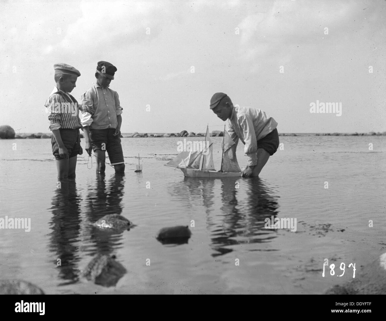 Three boys playing with a model sailing ship, 1897. Artist: Unknown Stock Photo