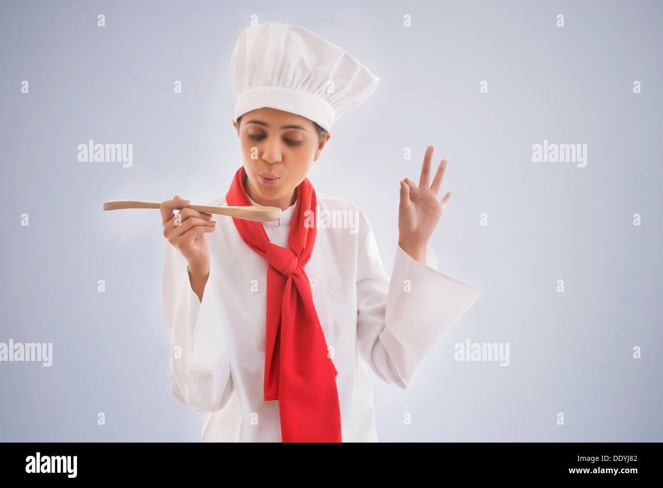 Young female chef tasting food isolated over gray background Stock Photo