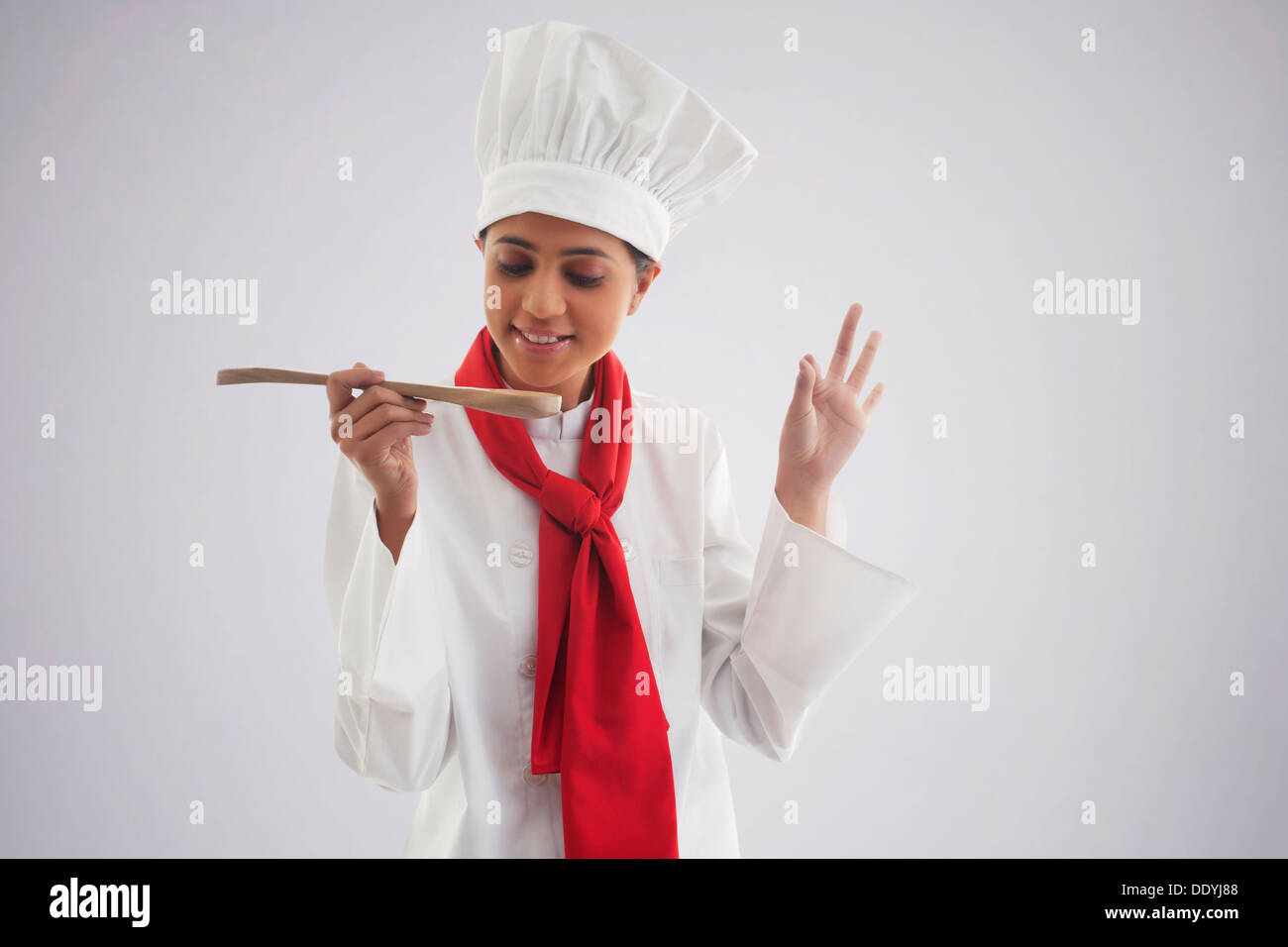 Female chef tasting food isolated over gray background Stock Photo