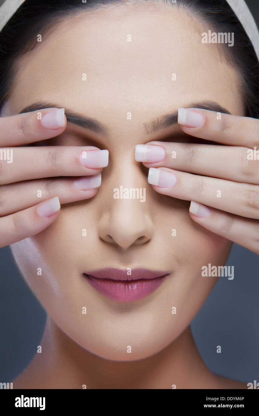 Head shot of a beautiful woman covering eyes with hands over colored background Stock Photo