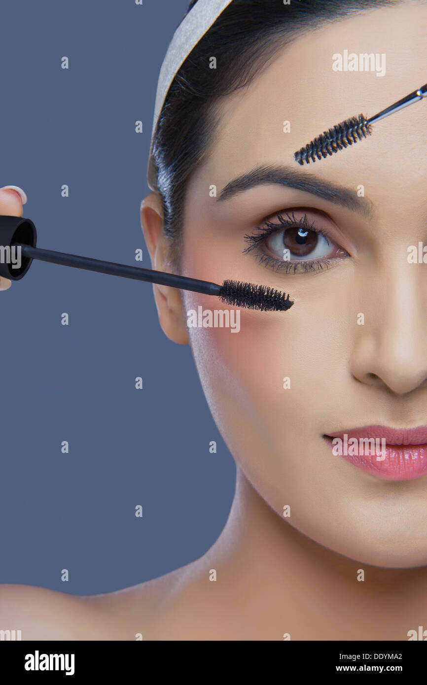 Cropped image of pretty young woman with mascara and eyebrow tinting applicator over colored background Stock Photo