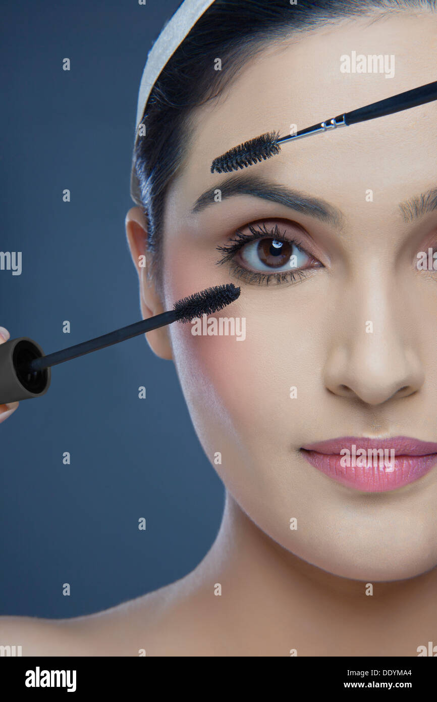 Cropped image of an attractive young woman with mascara and eyebrow tinting applicator over colored background Stock Photo