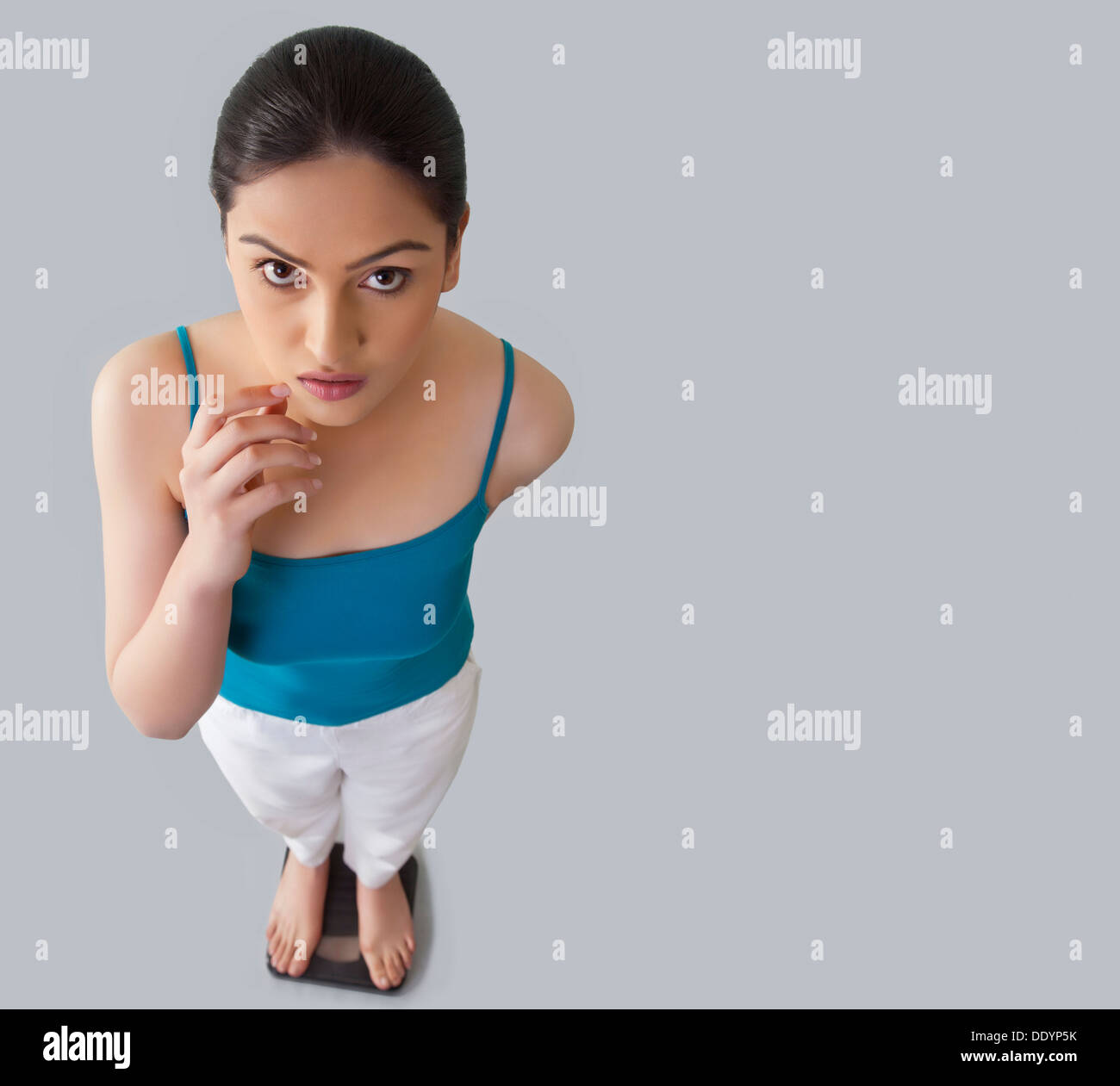 https://c8.alamy.com/comp/DDYP5K/portrait-of-worried-young-woman-standing-on-weighing-scale-against-DDYP5K.jpg