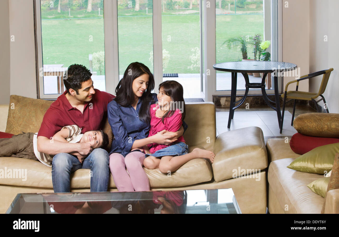 Happy young couple sitting with kids on sofa at home Stock Photo