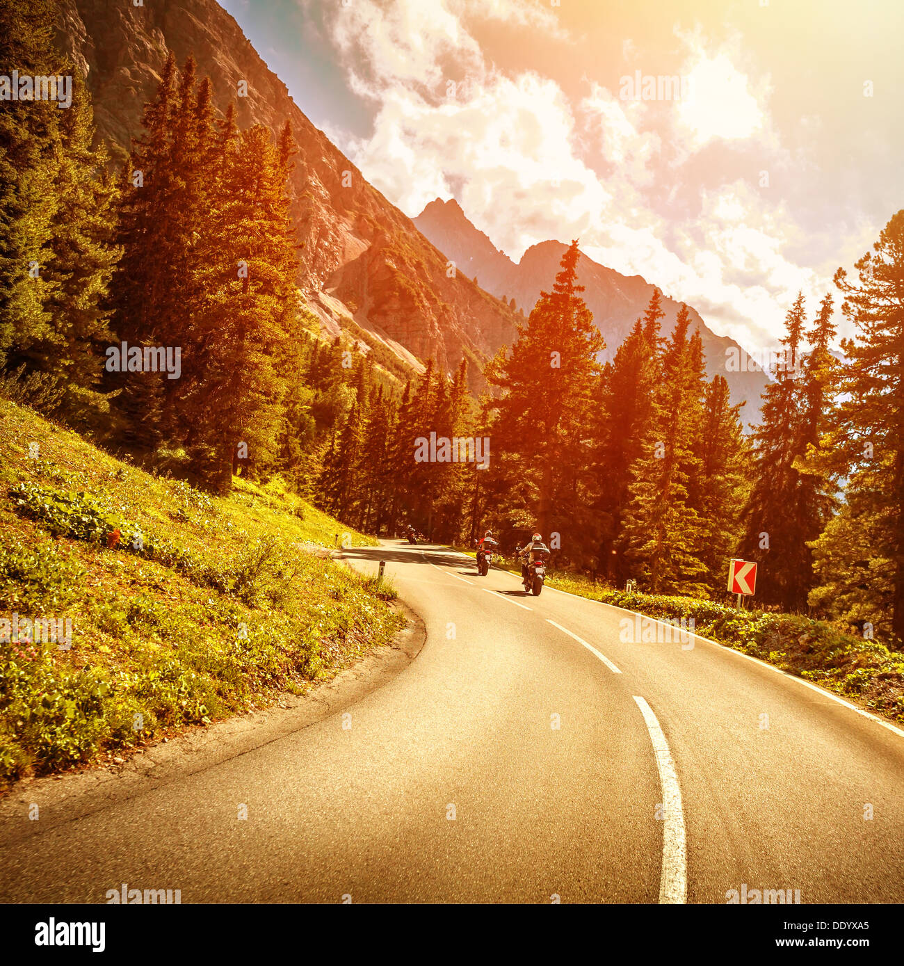 Motorcyclists on the mountainous road in bright red sunset light, riding on highway pass along Alpine mountains Stock Photo