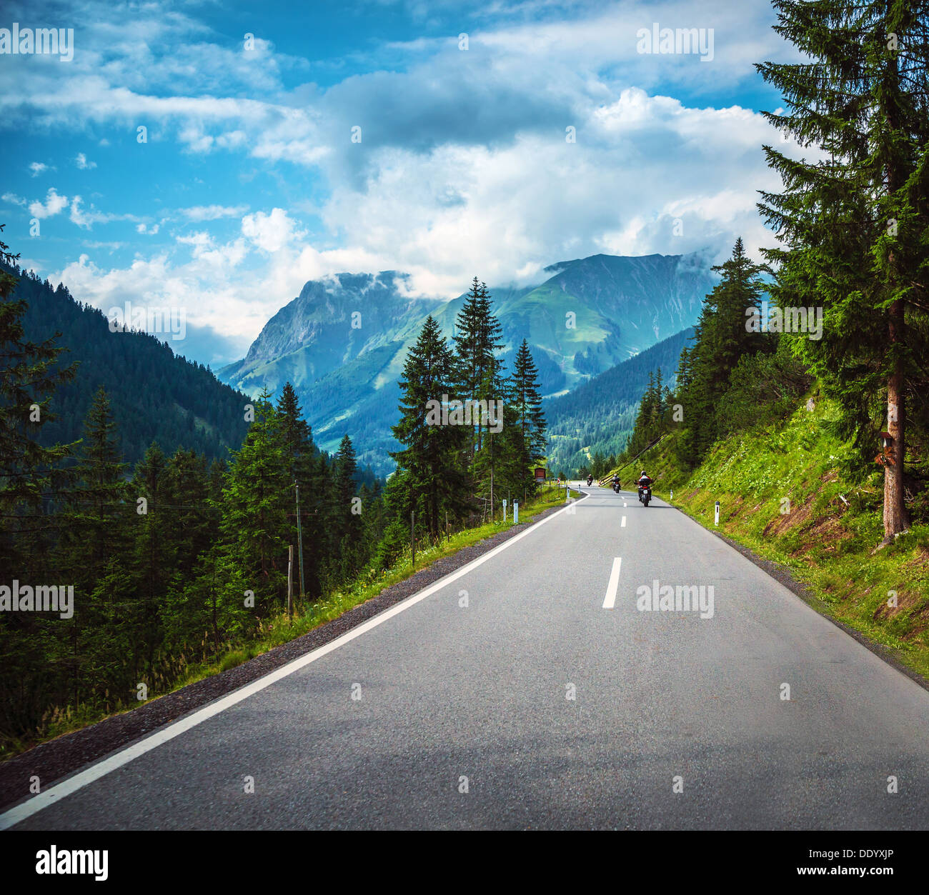 Group of bikers riding on road pass along Alpine mountains, travelers in Europe, mountainous highway, pine tree forest Stock Photo