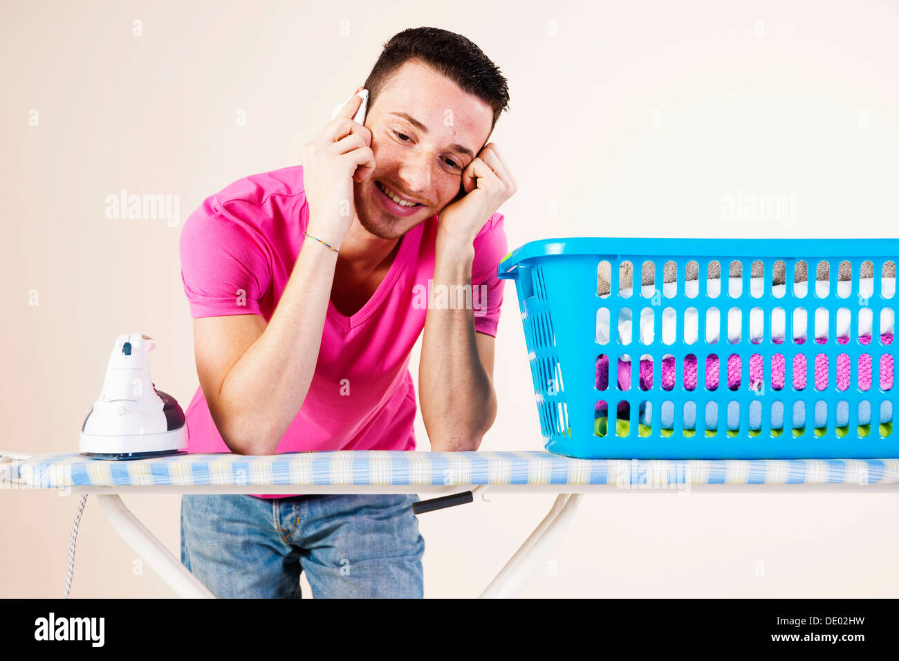 Young man talking on the telephone while leaning on an ironing board Stock Photo