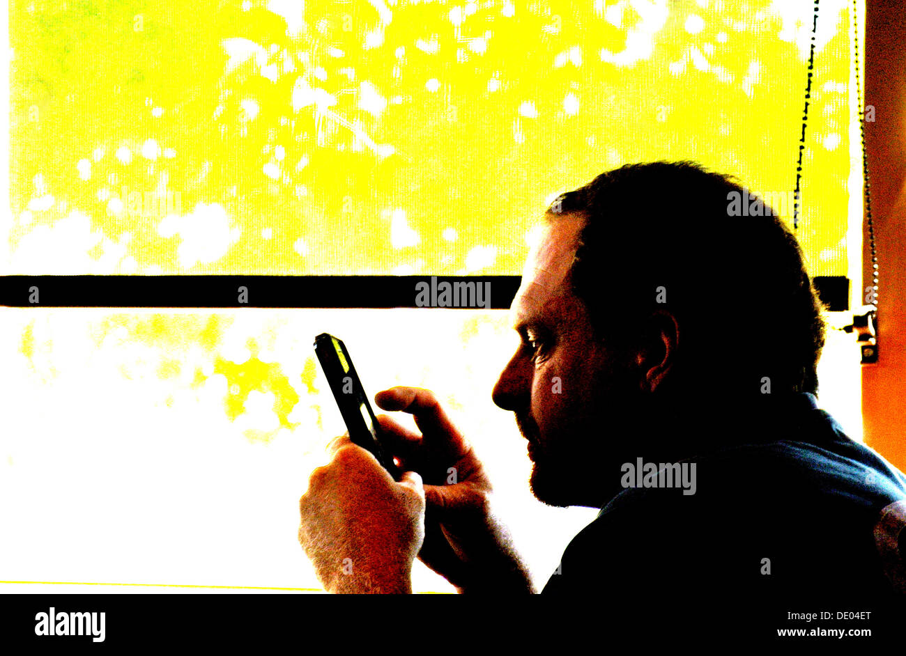 close up of man texting on an iphone silhouetted against a window in Cafe Stock Photo