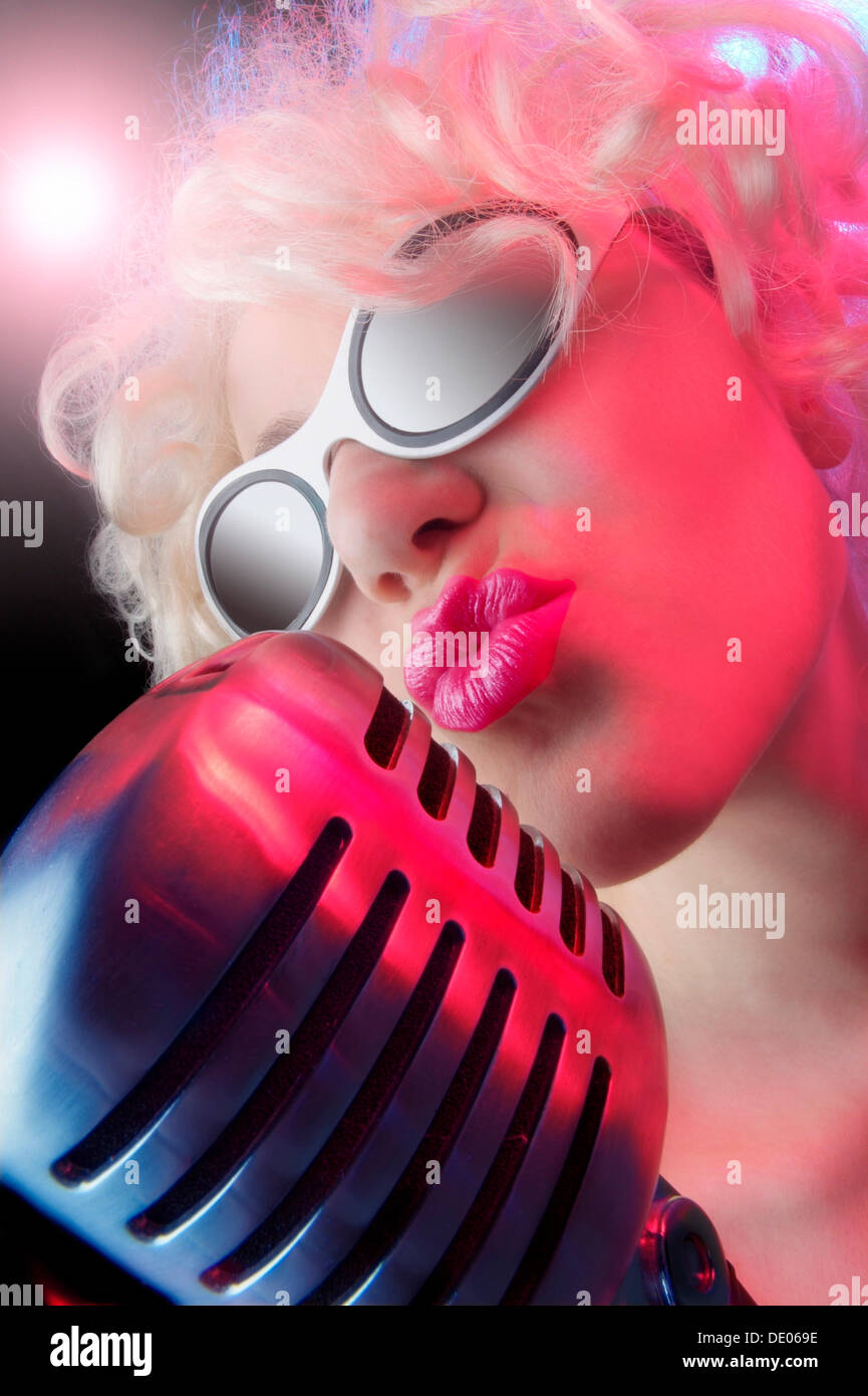 Woman wearing sunglasses and singing into a microphone Stock Photo