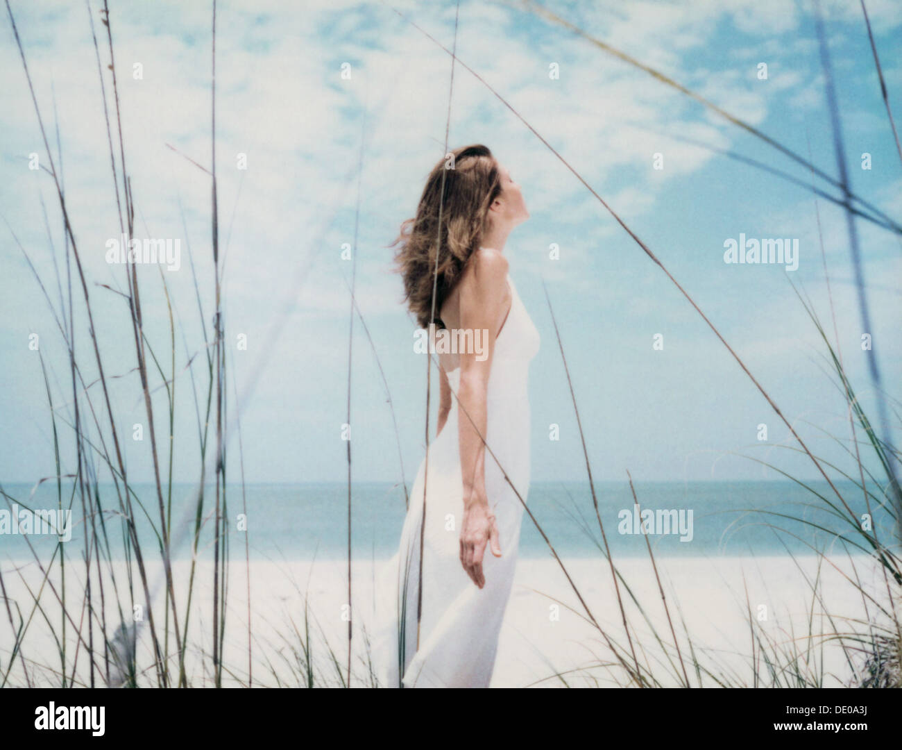 Woman standing at the beach with arms back, side view Stock Photo