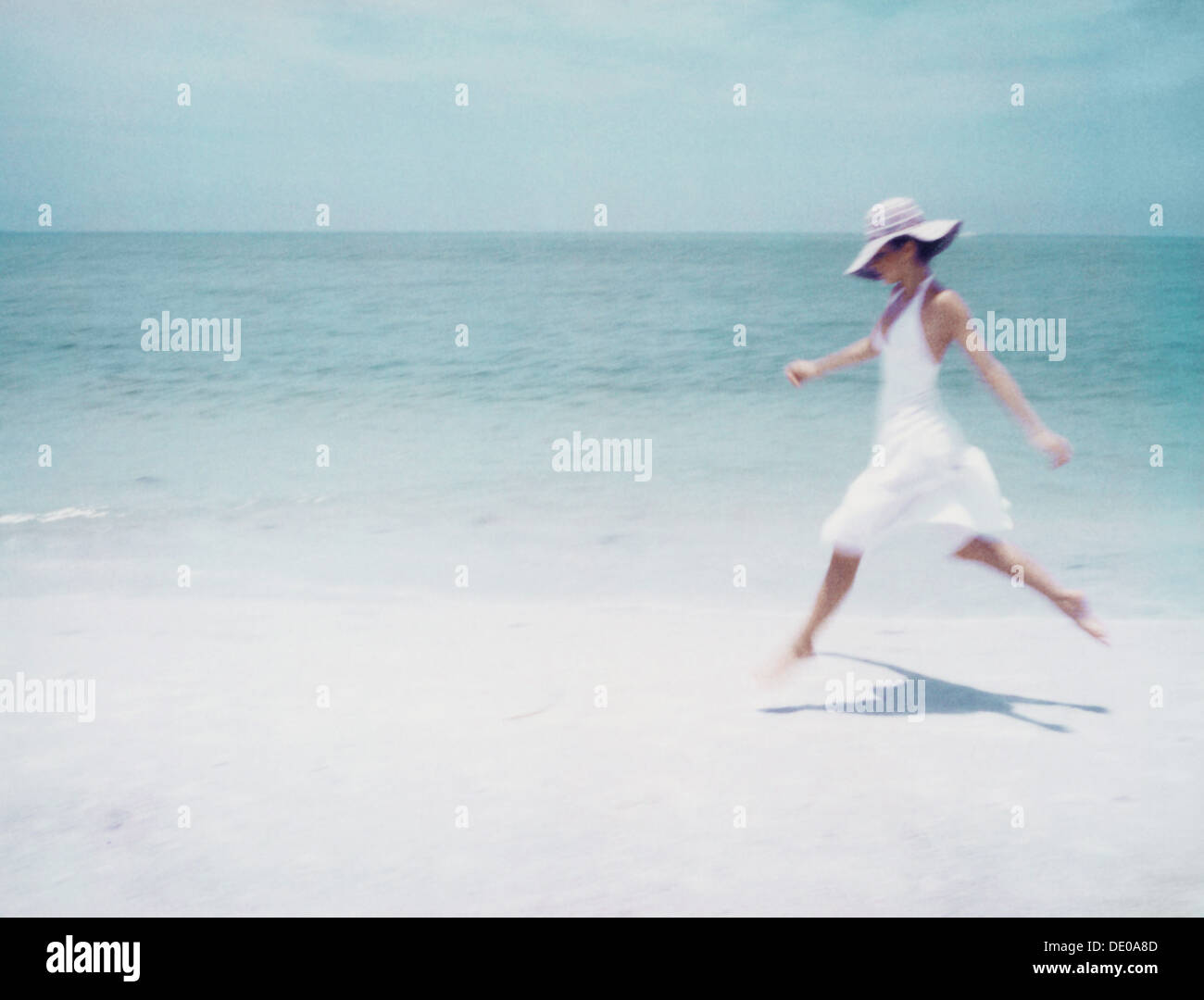 Young woman in dress and sun hat, running on beach, side view Stock Photo