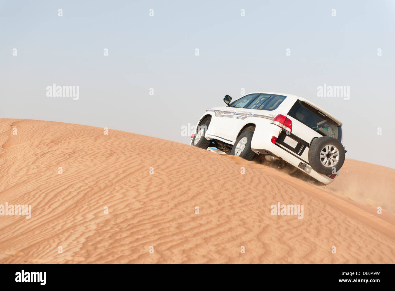 Sports utility vehicle driving up desert sand dune Stock Photo