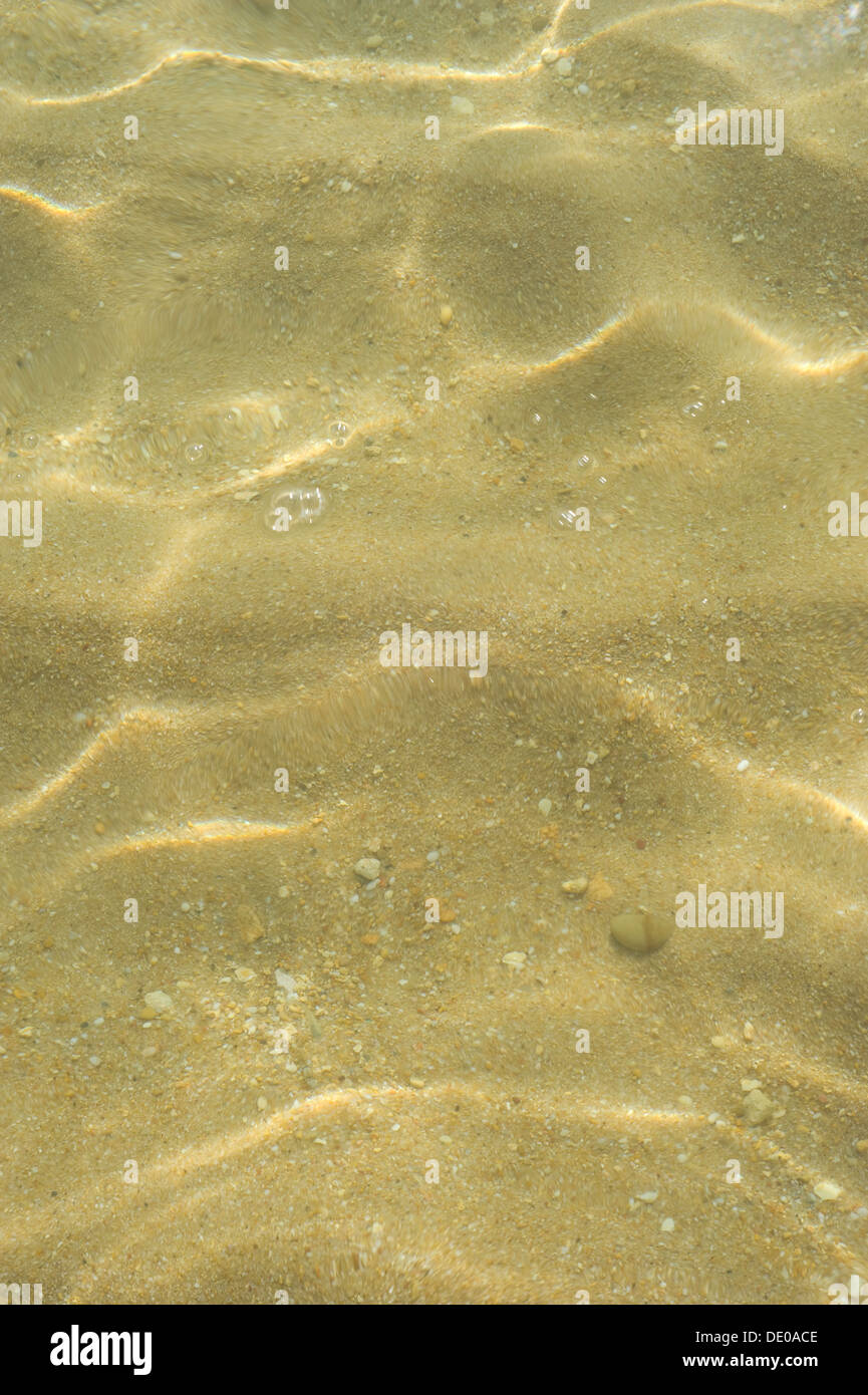 Patterns of rippling sunlight on shallow sea water on a sandy shore. Stock Photo