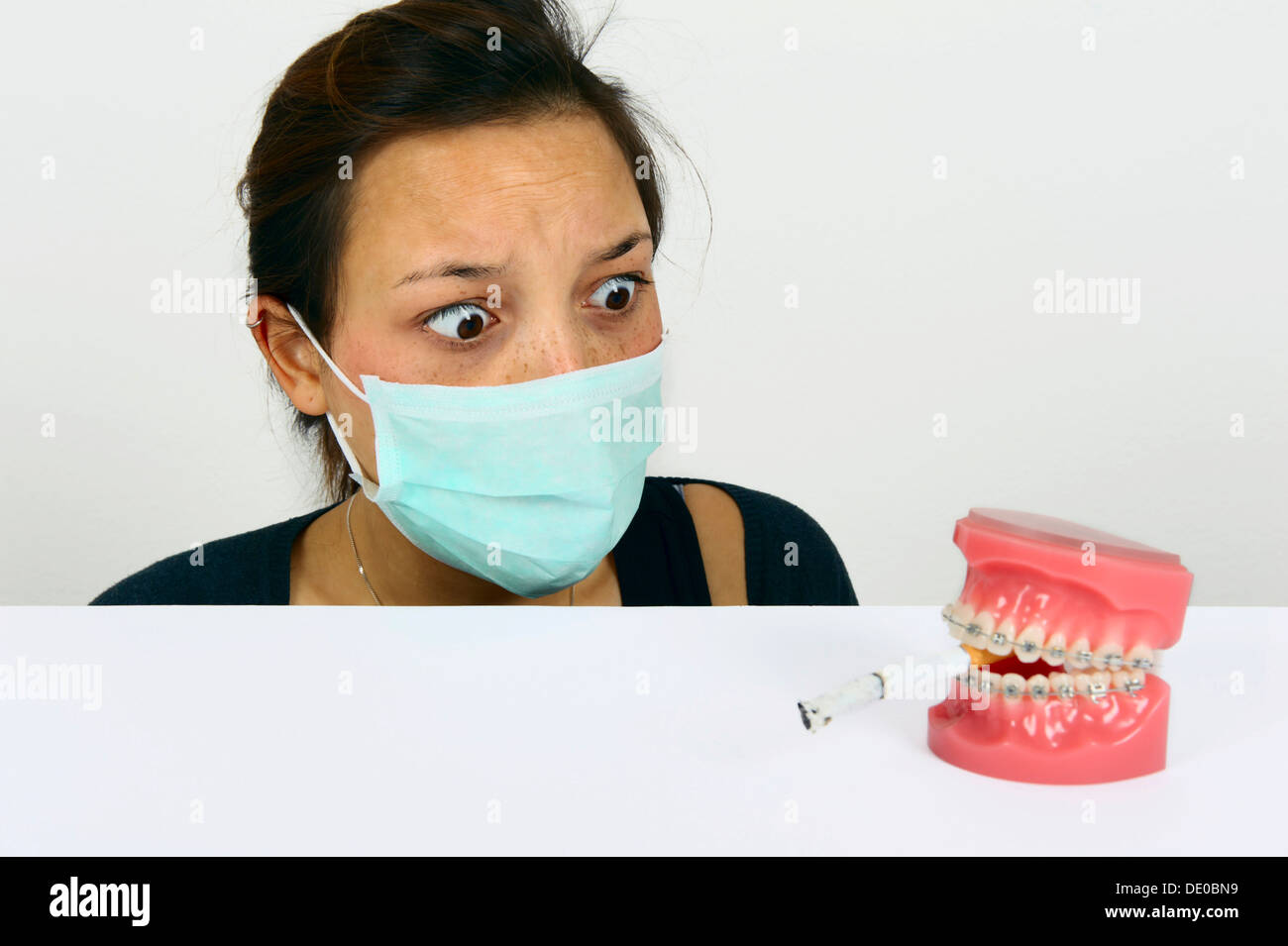 Symbolic image for adolescent smokers, young woman looking in horror at dentures with fixed braces and a smoking cigarette Stock Photo