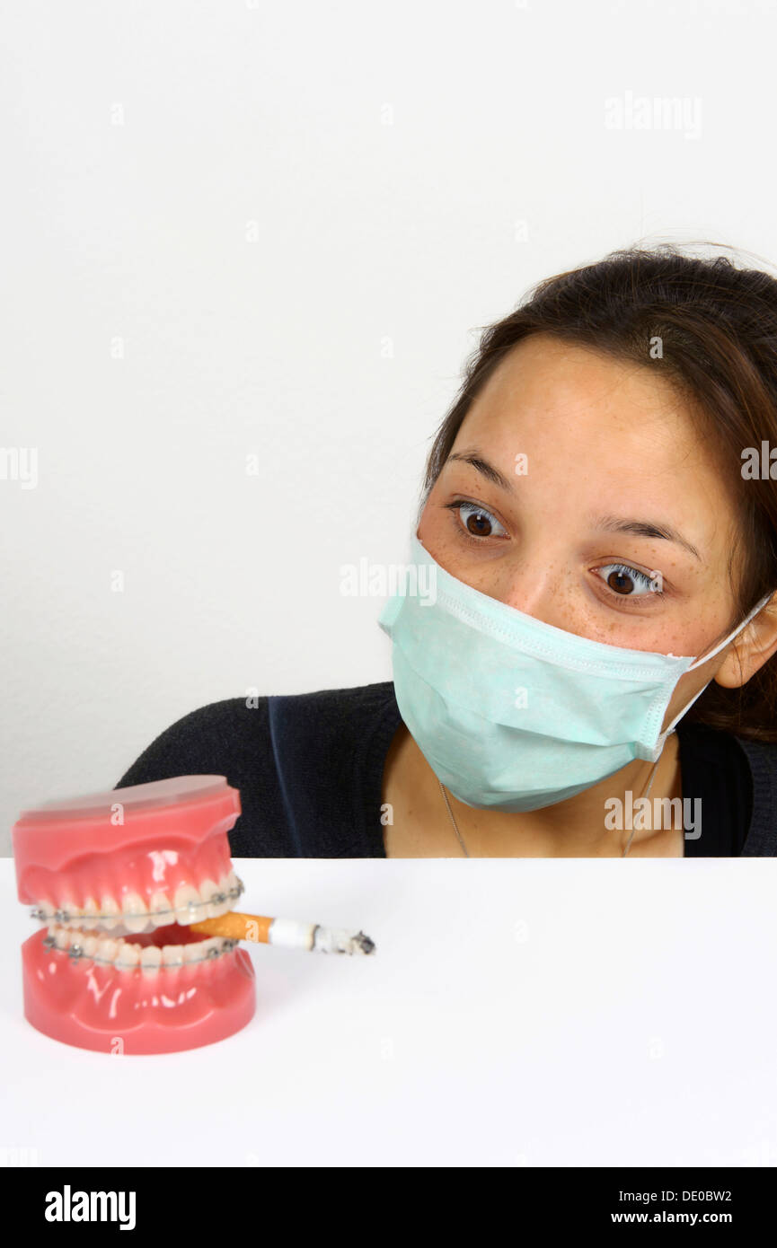 Symbolic image for adolescent smokers, young woman looking in horror at dentures with fixed braces and a smoking cigarette Stock Photo