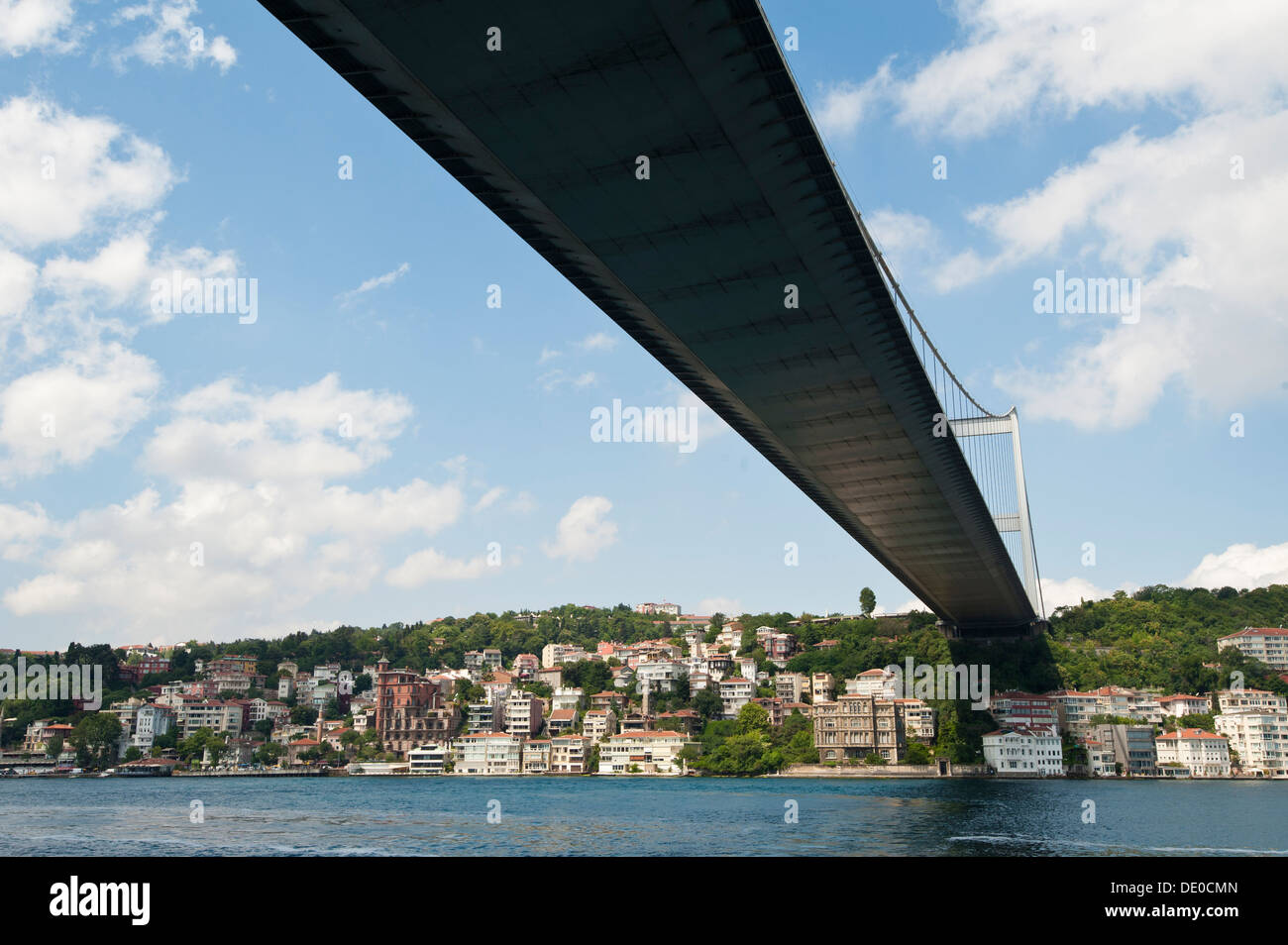 Large suspension road bridge over a river against a blue sky background with residences underneath Stock Photo