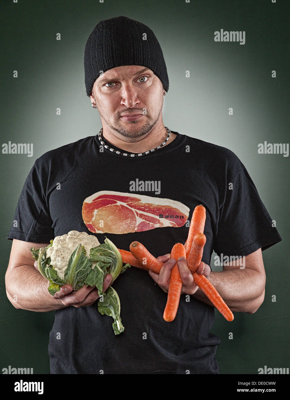 Man with a meat image on his T-shirt holding cauliflower and carrots in his hands Stock Photo