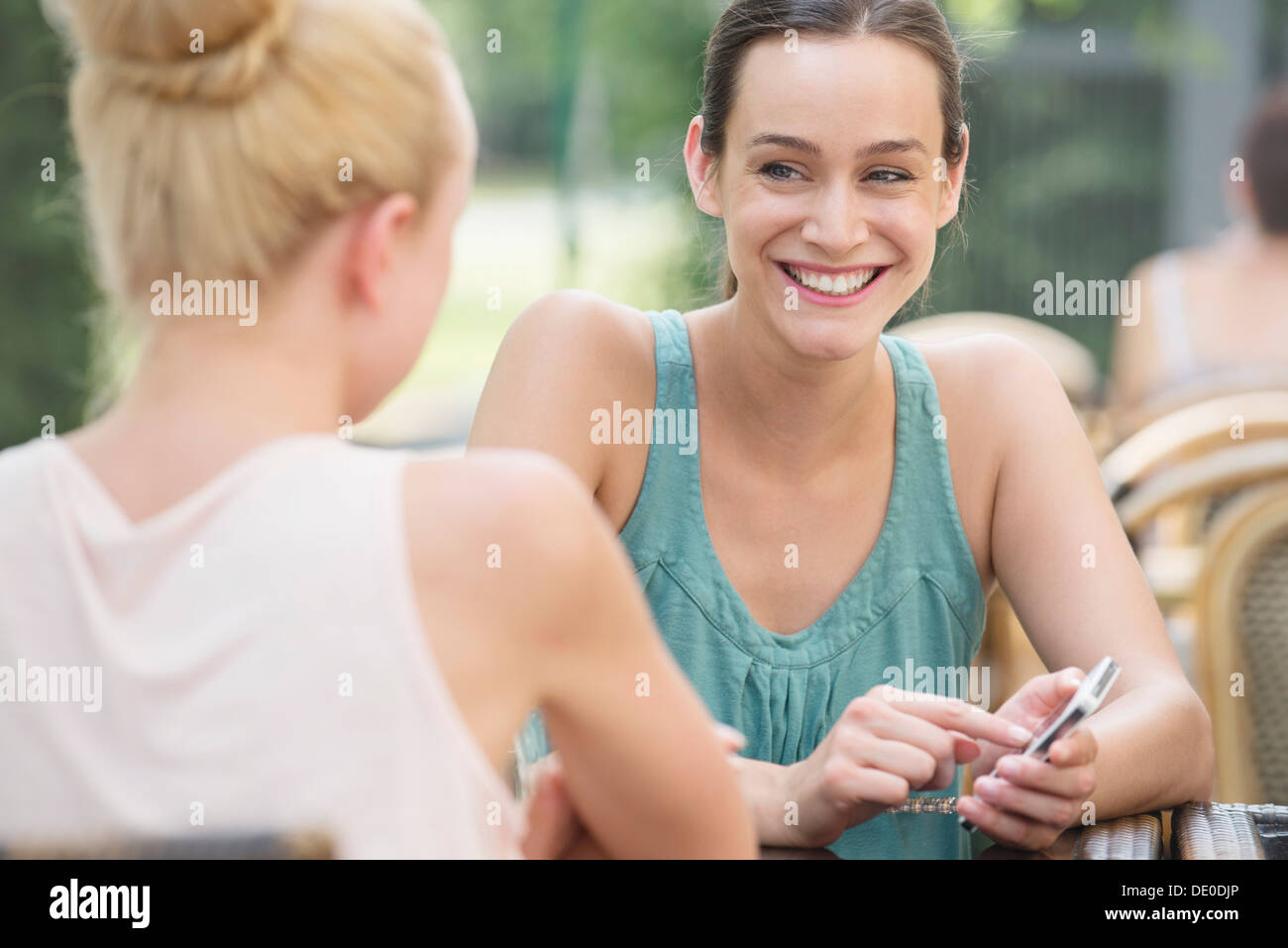 Women chatting outdoors, one woman holding smartphone Stock Photo