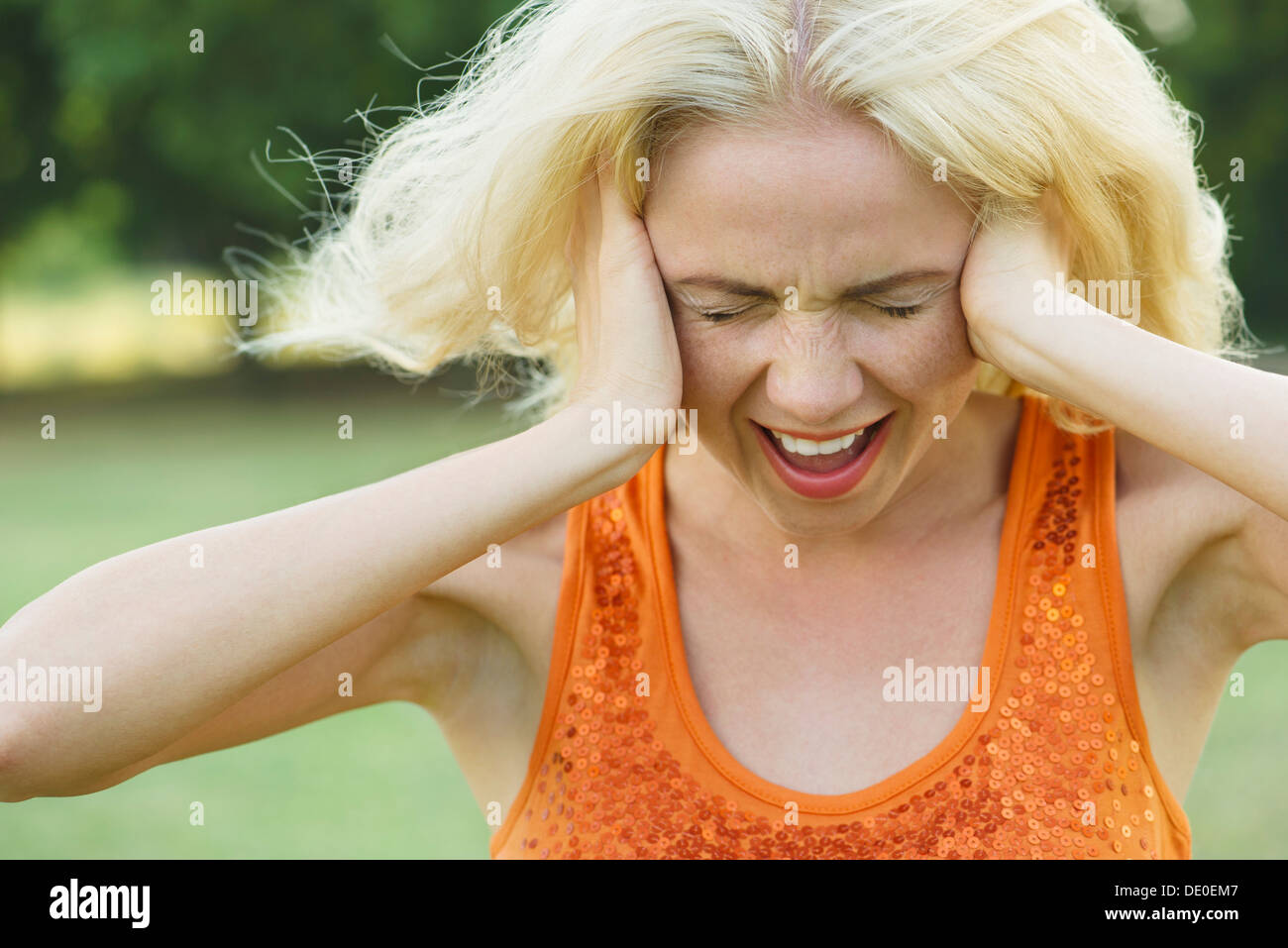 Woman screaming with eyes closed and hands over ears Stock Photo