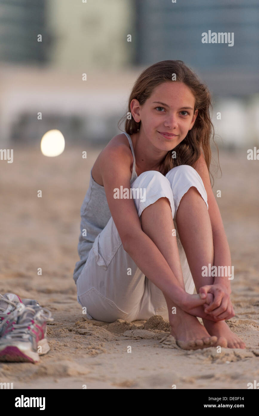 Preteen girl sitting on beach with barefeet, hugging knees Stock Photo