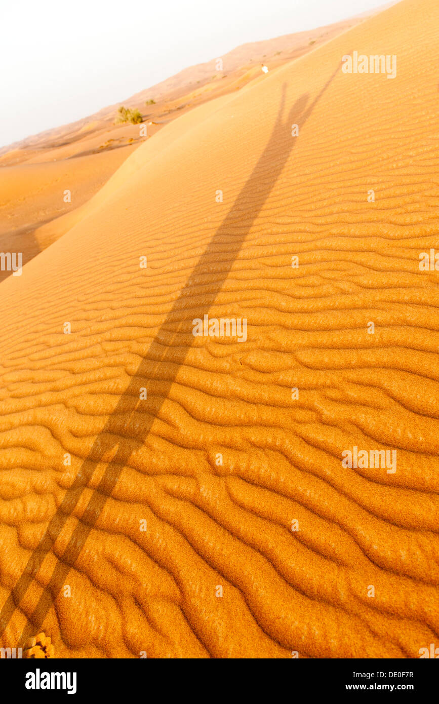 Shadow of person with arms raised cast on desert sand Stock Photo