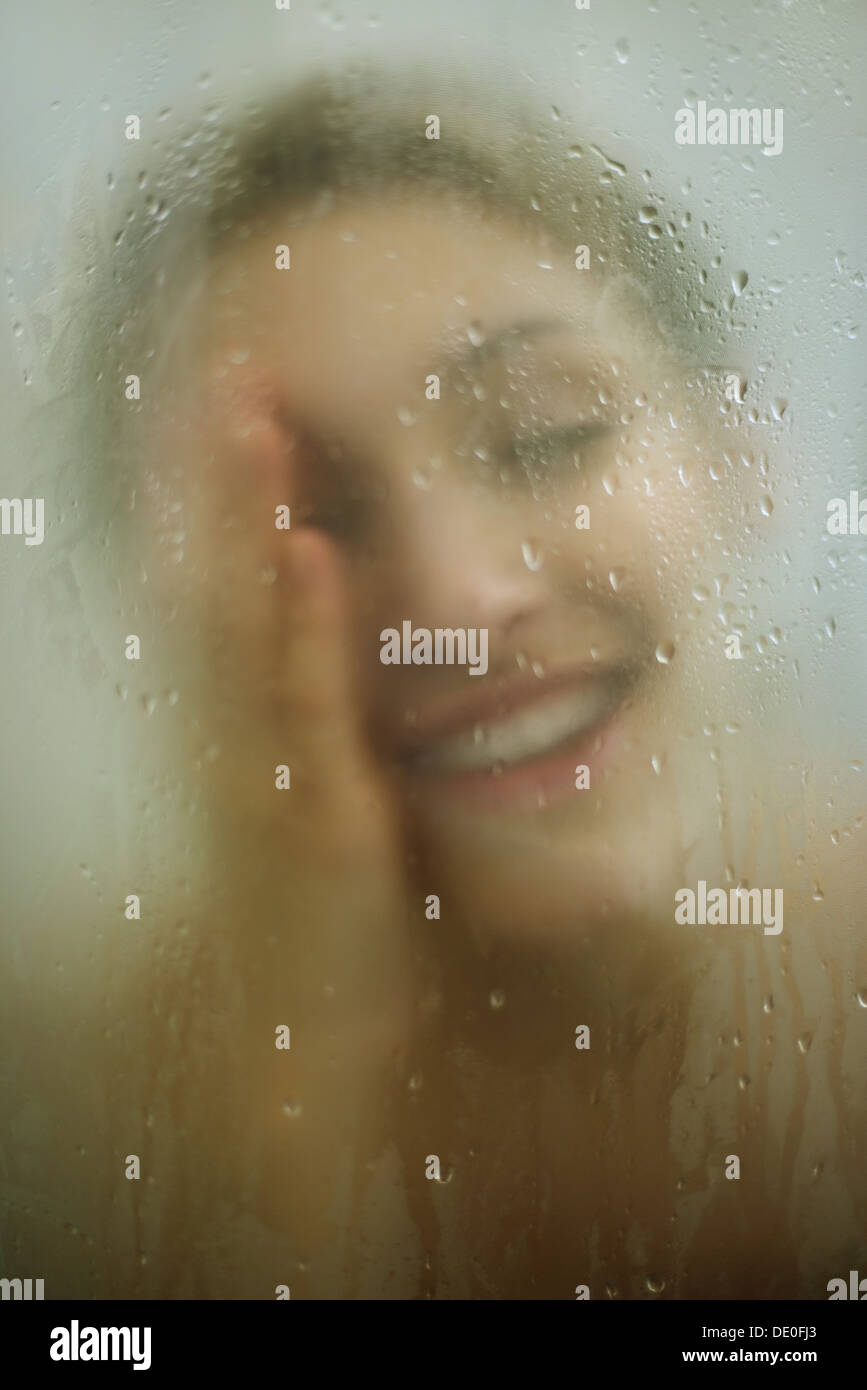 Woman behind shower door, wiping face Stock Photo