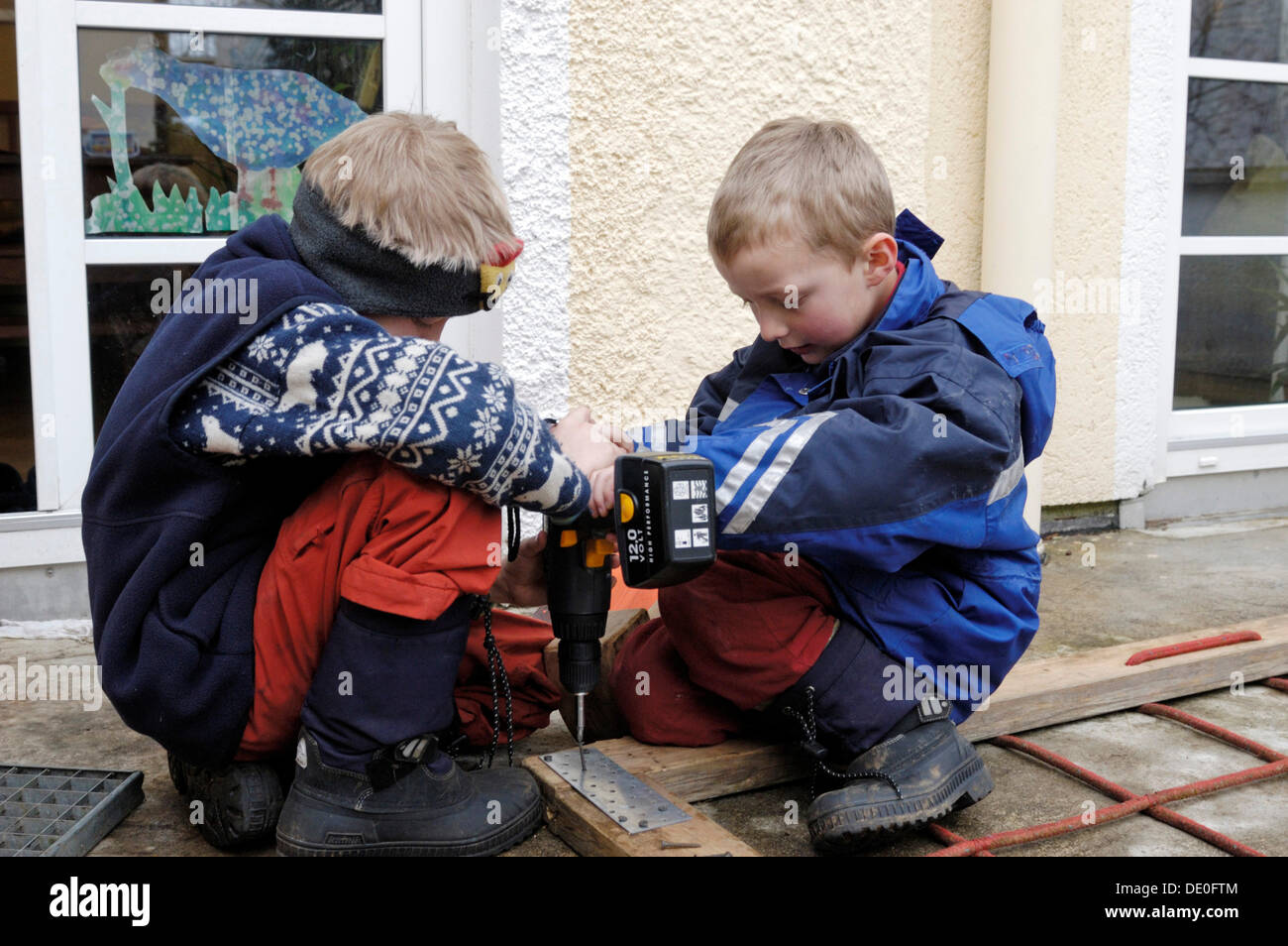 Two small boys, 7 and 9, screwing a screw into a wooden frame with a cordless screwdriver Stock Photo