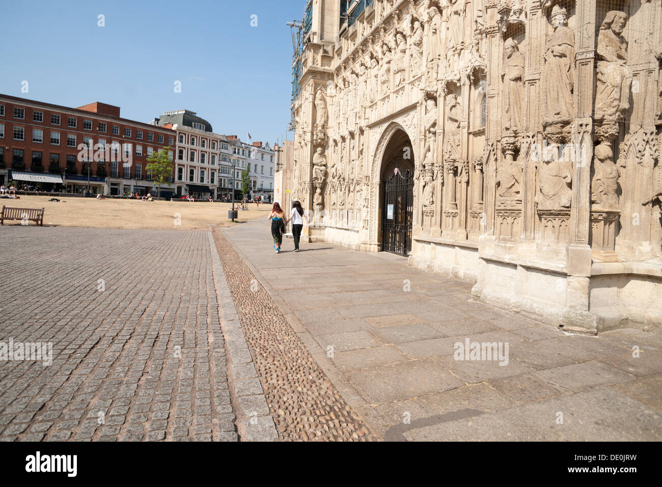 Two people walk along the path outside the intricately carved exterior wall of the Exeter Cathedral. Church of Saint Peter. Stock Photo