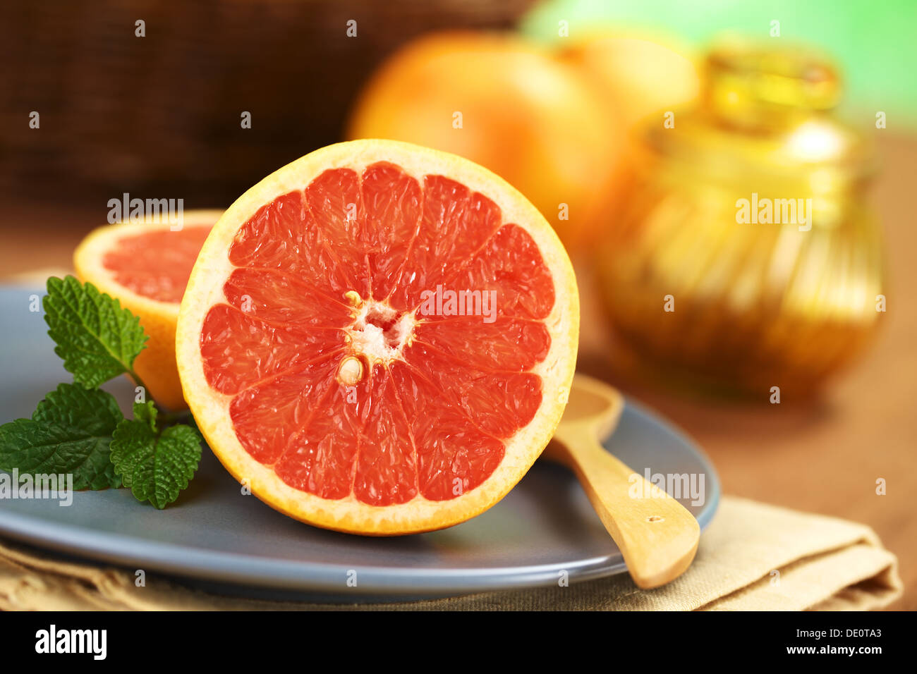 Half of a pink-fleshed grapefruit on blue plate with mint leaf and wooden spoon Stock Photo