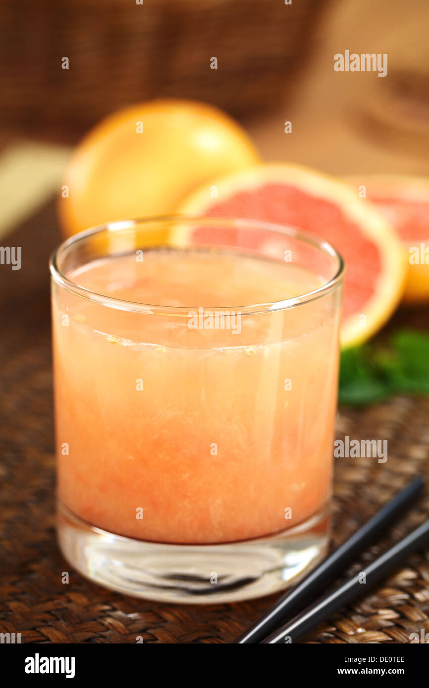 Freshly squeezed juice of the pink-fleshed grapefruit with black drinking straws on the side and grapefruits in the back Stock Photo