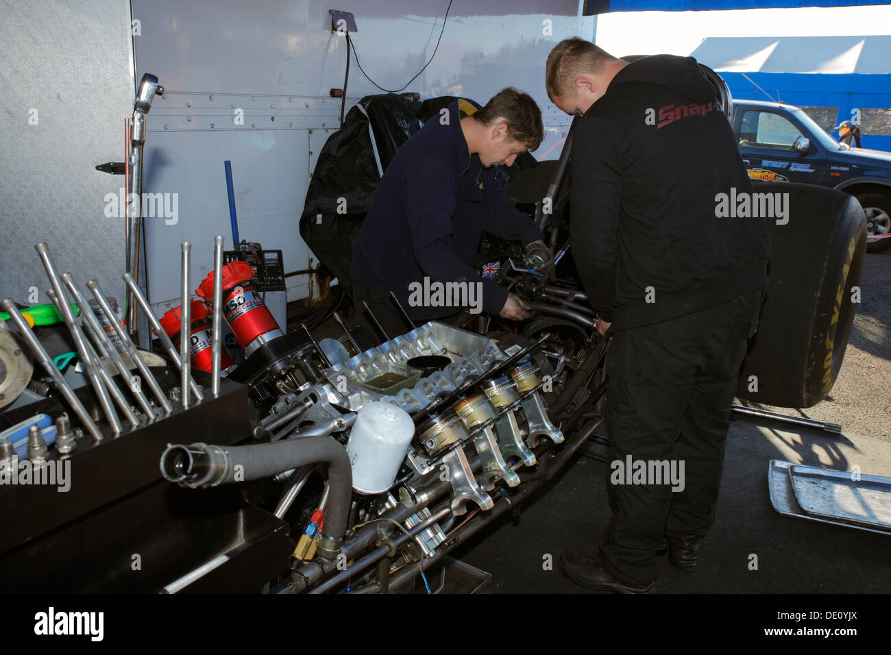 Mechanics working on their Ford Mustang Top fuel funny car dragster after an engine explosion at Santa Pod pits. Stock Photo