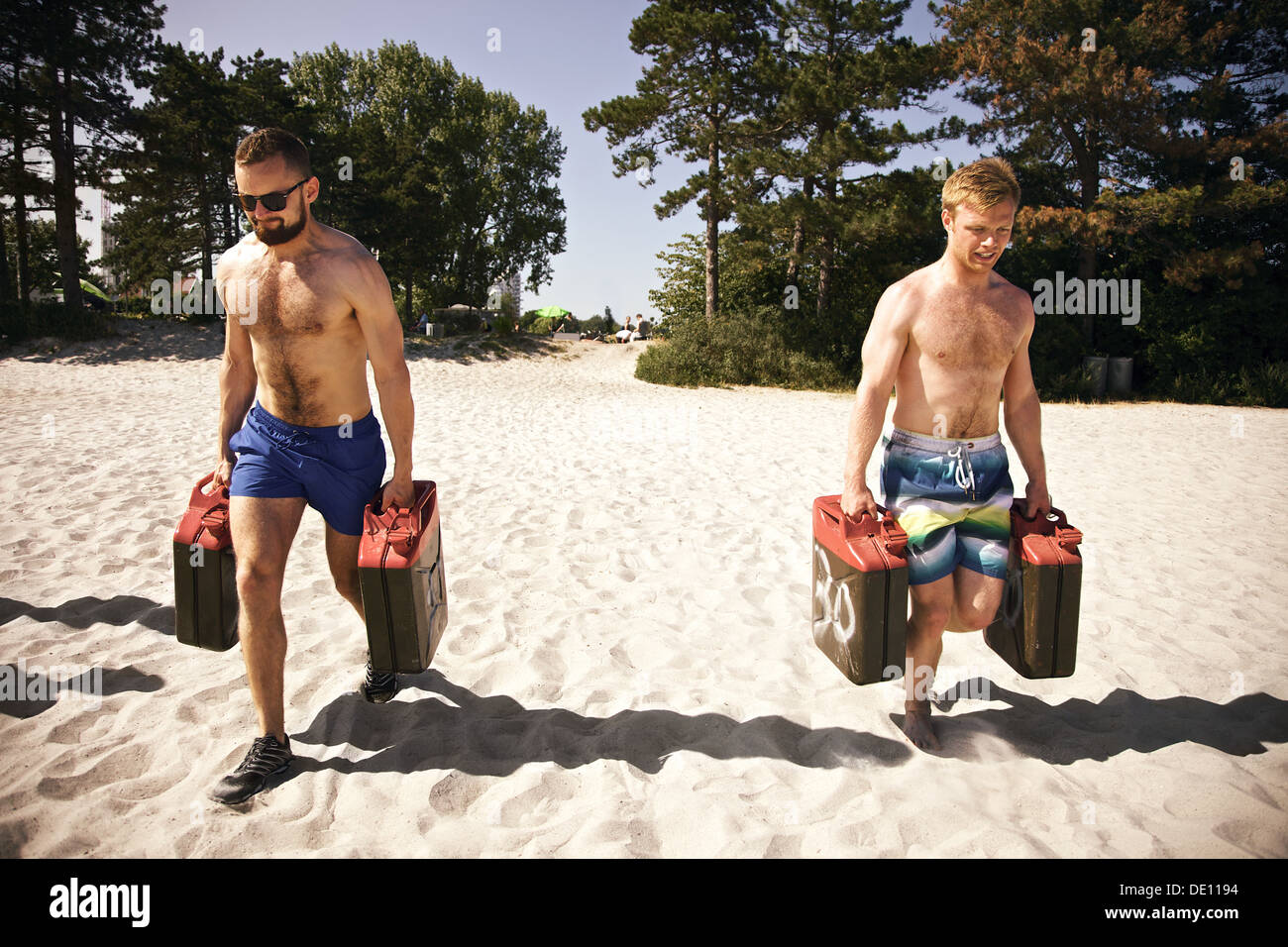 Two tough young male crossfitters lifting heavy jerrycans and walking during a crossfit workout on the beach. Stock Photo