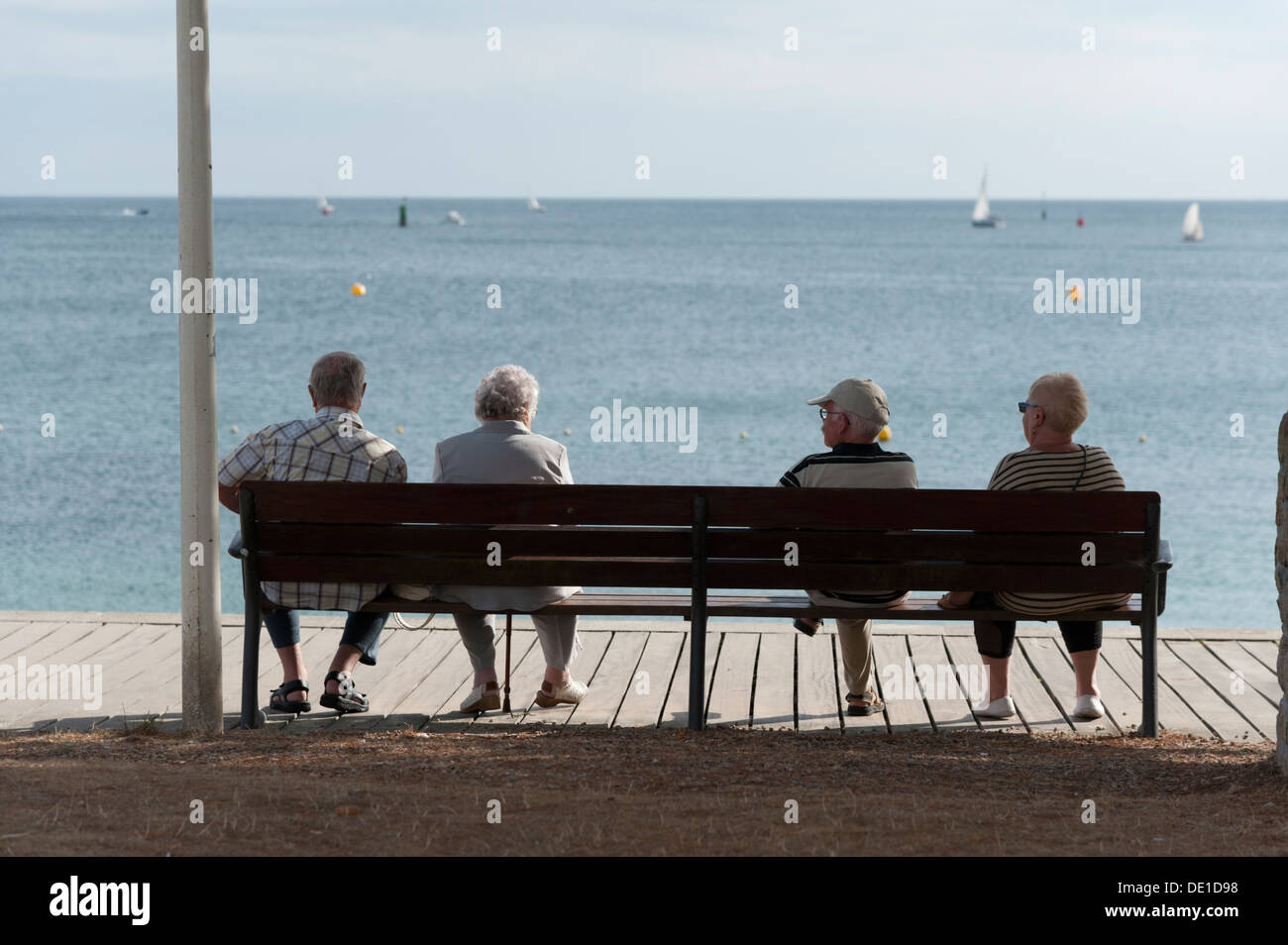 Rear view of four older people sitting on a bench at the seaside at Benodet Brittany France Stock Photo