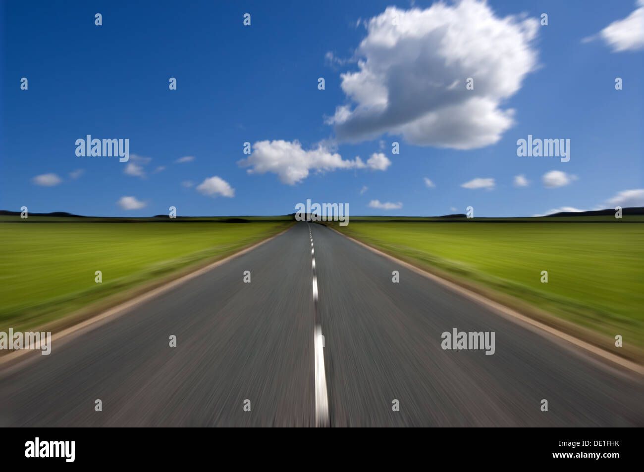Rural road stretching out into the distance with motion blur under a big expanse of blue sky. Stock Photo
